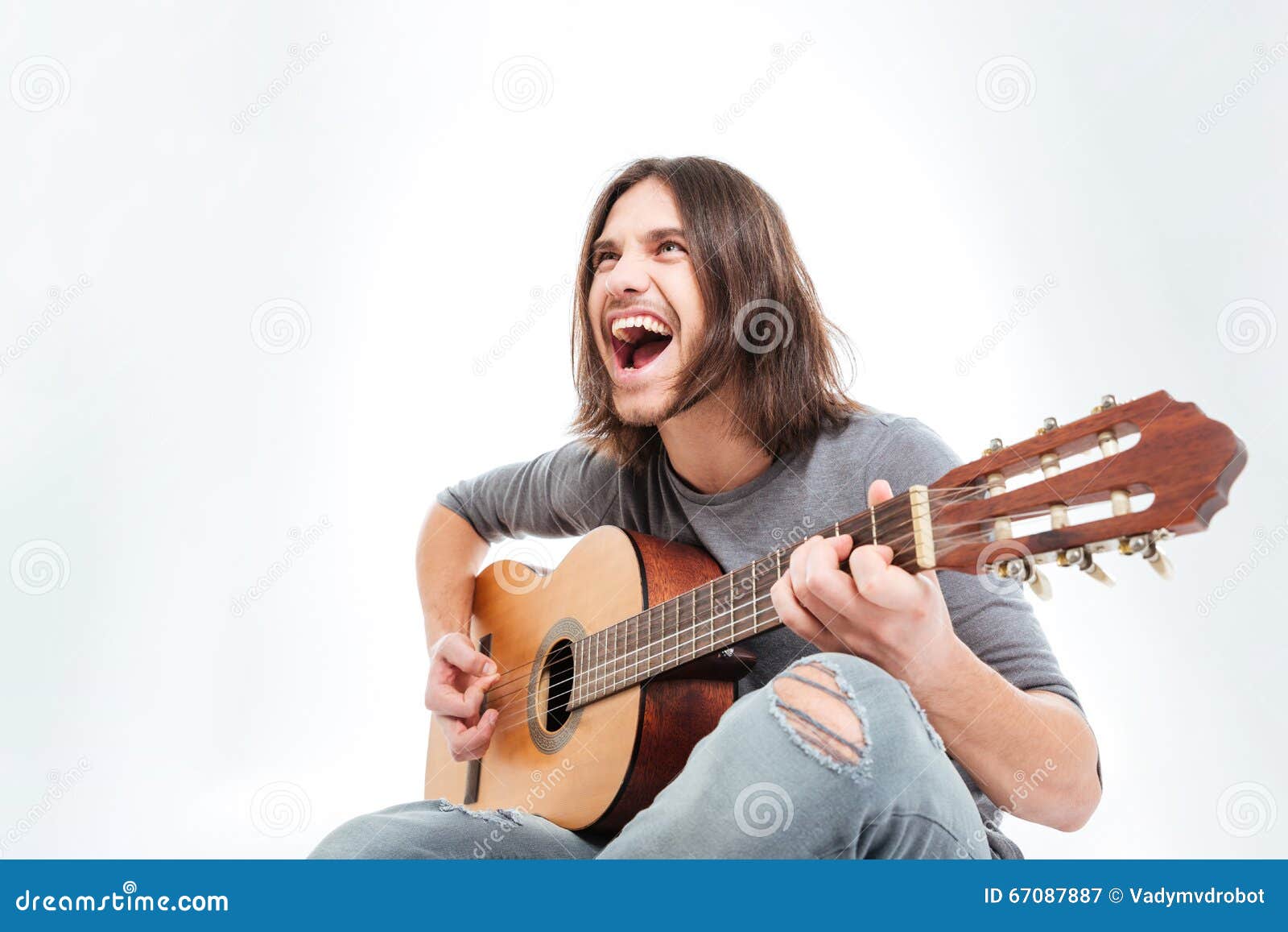 Giovane felice con capelli lunghi che giocano chitarra e che cantano sopra il fondo bianco