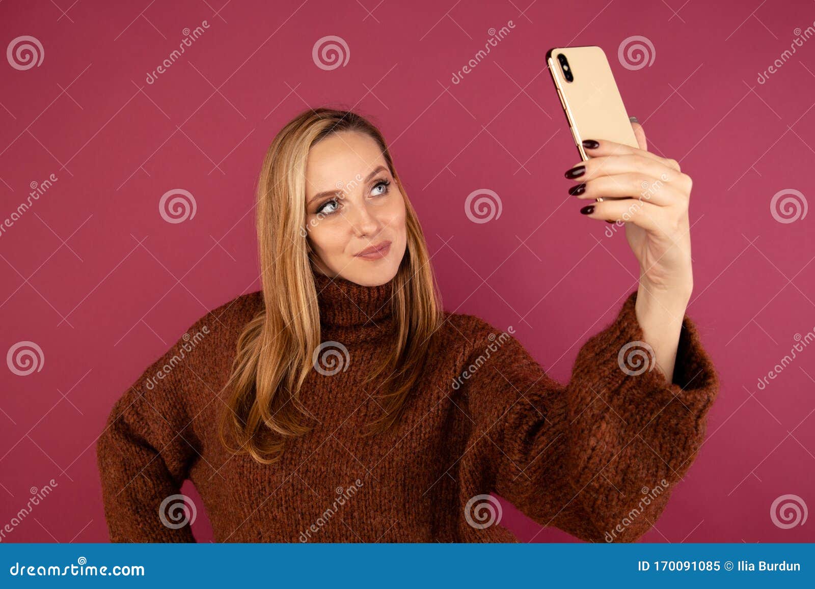 Giovane signora in maglione che si fa fotografare al telefono nello studio rosa