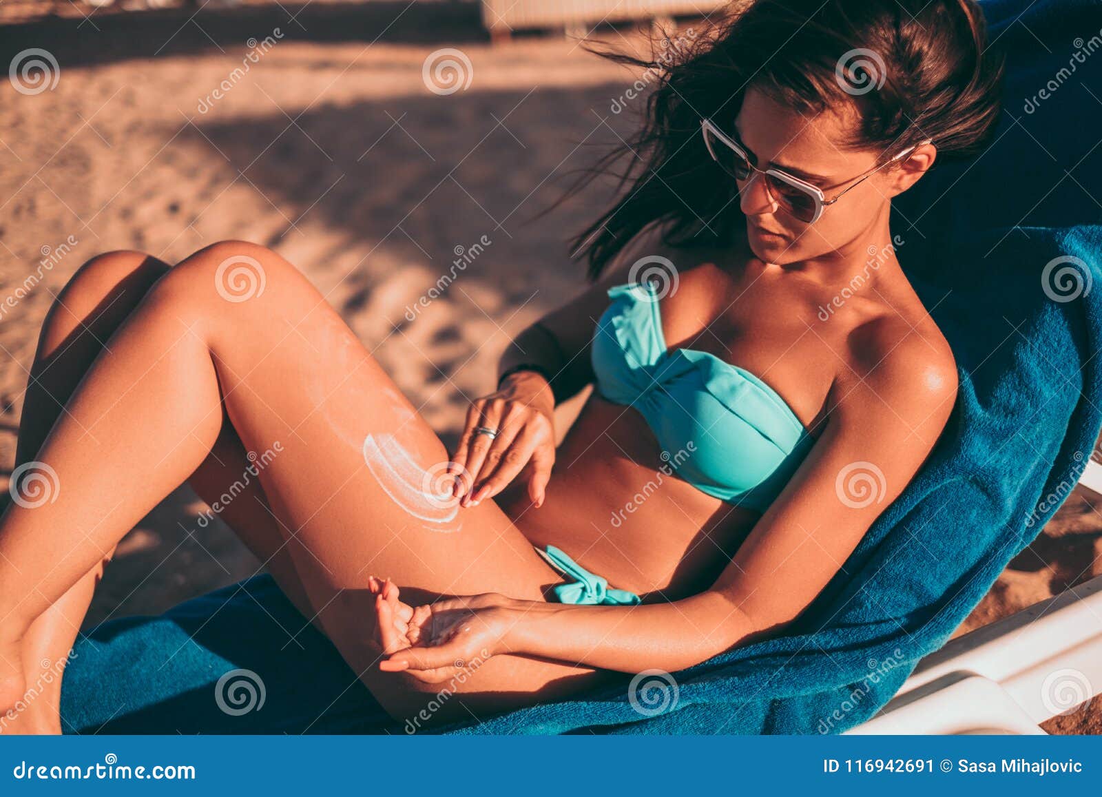 girl applying sunscreen while lying on the on the beach
