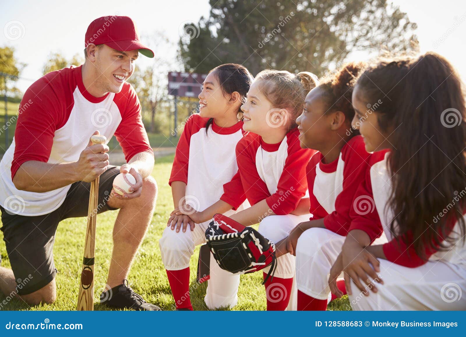 Girl Baseball Team Kneeling in a Huddle with Their Coach Stock Image
