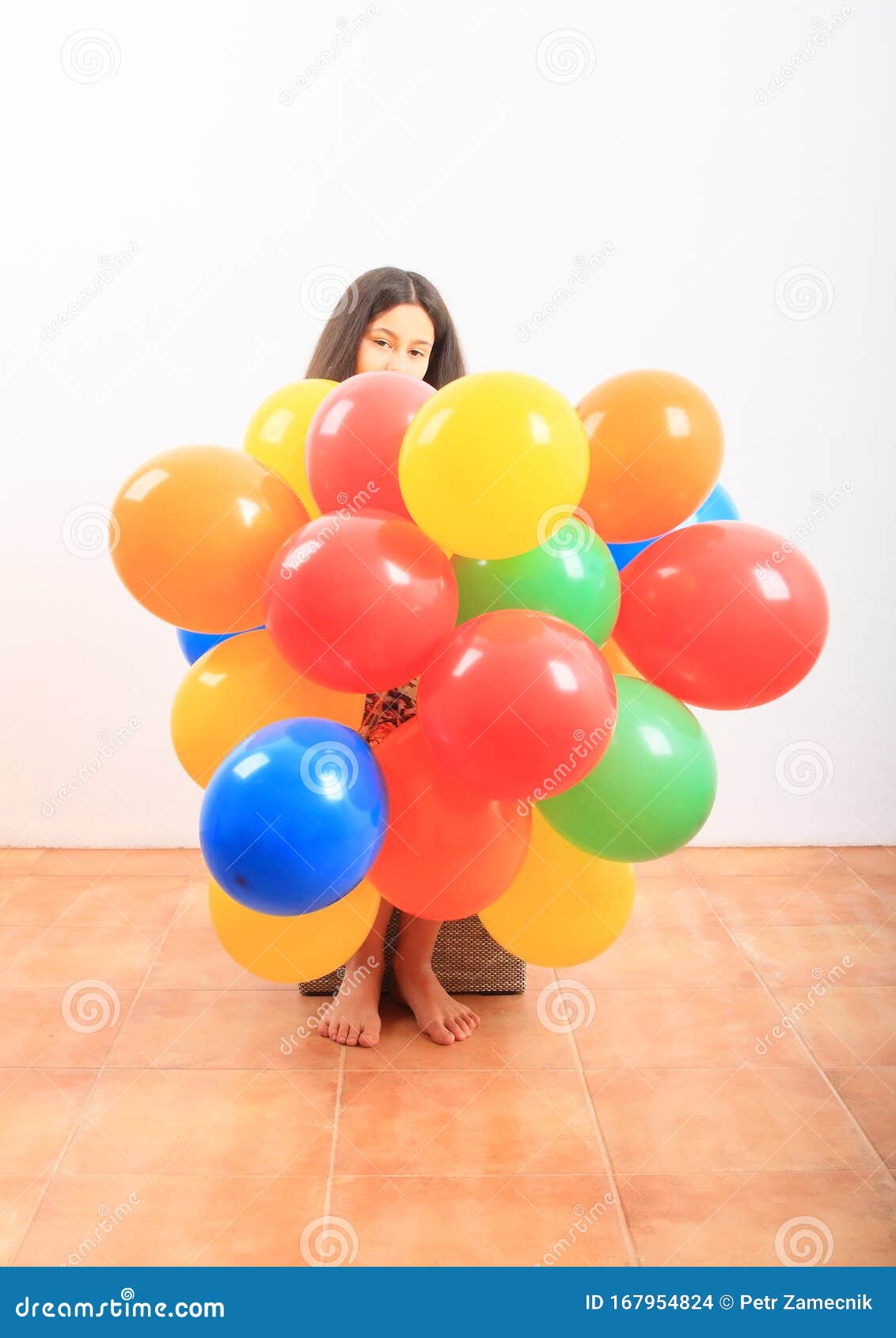 Girl behind inflating balloons. Barefoot girl - teenage kid sitting behind colorful inflated balloons. Childhood concept.