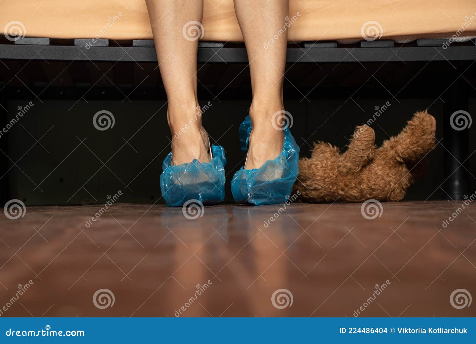 A Girl in Black High-heeled Shoes in Blue Shoe Covers on the Floor Laid the Bed Under the Bed is a Childrenand X27;s Teddy Bear Stock Photo