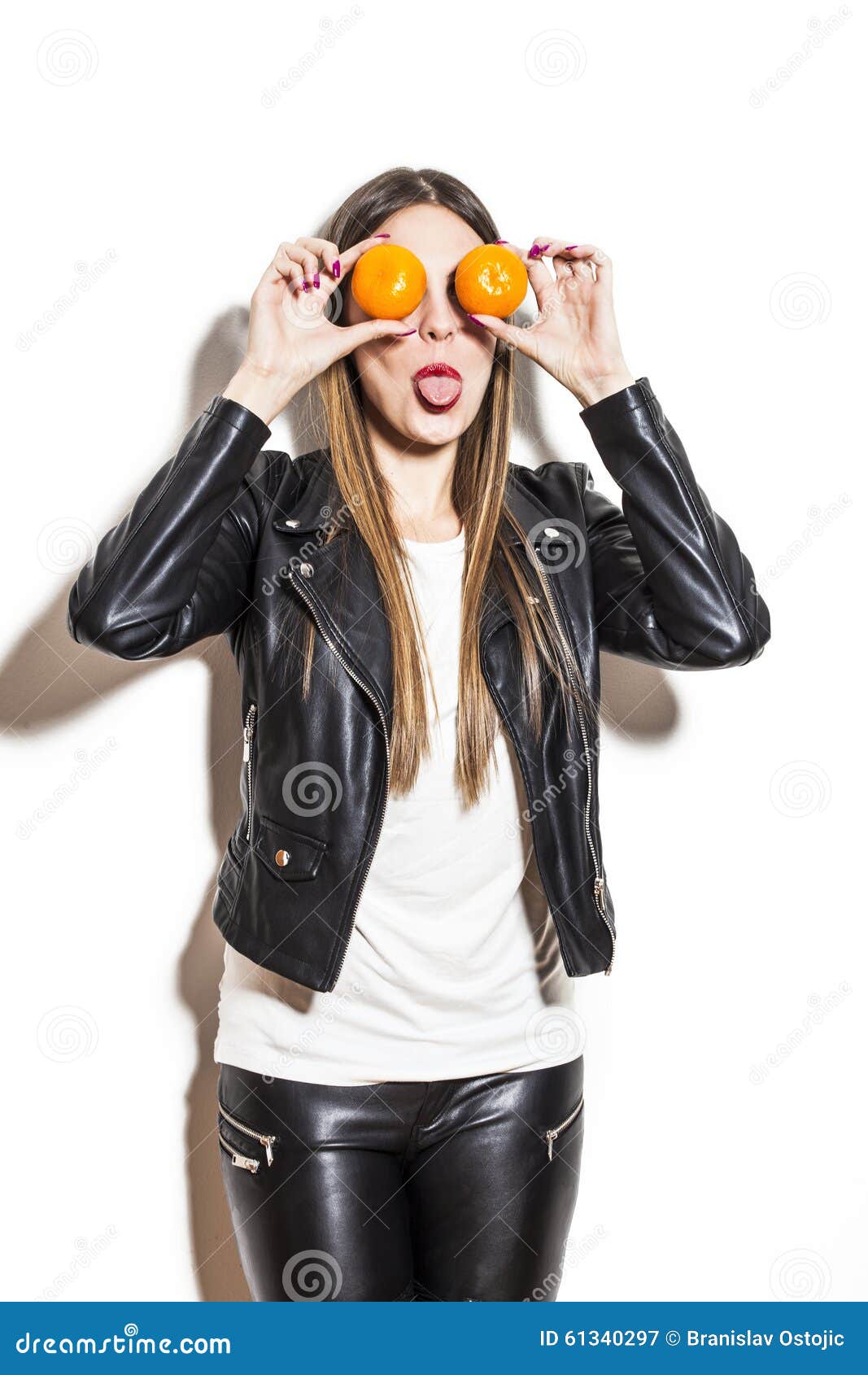 Girl clowning around. Young woman with tangerines on her eyes making fun, wearing black leather jacket and leggings, studio white