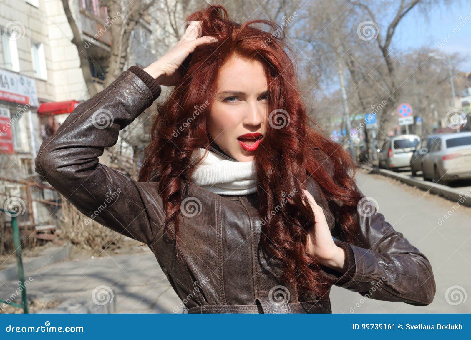 Pleased red haired female with curly hair wears sunglasses and dress poses  near door of ancient building holds hands together enjoys rest in open  air likes viewing old historic famous places 8168305