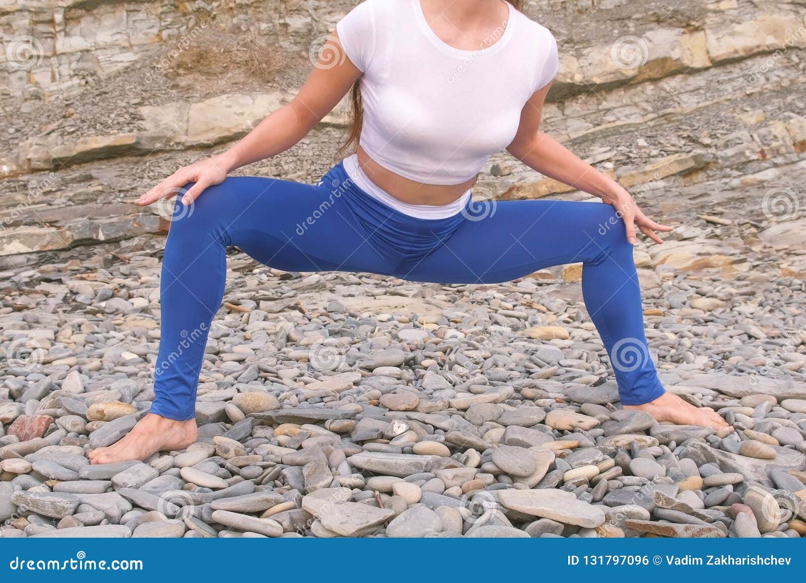 girl is doing plie squats the bodyflex during breathing exercises on the rock background. close-up belly and body