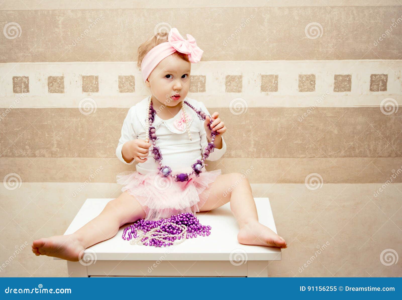 A Girl Dressed Up Like A Doll Sits On A Chest Of Drawers Stock