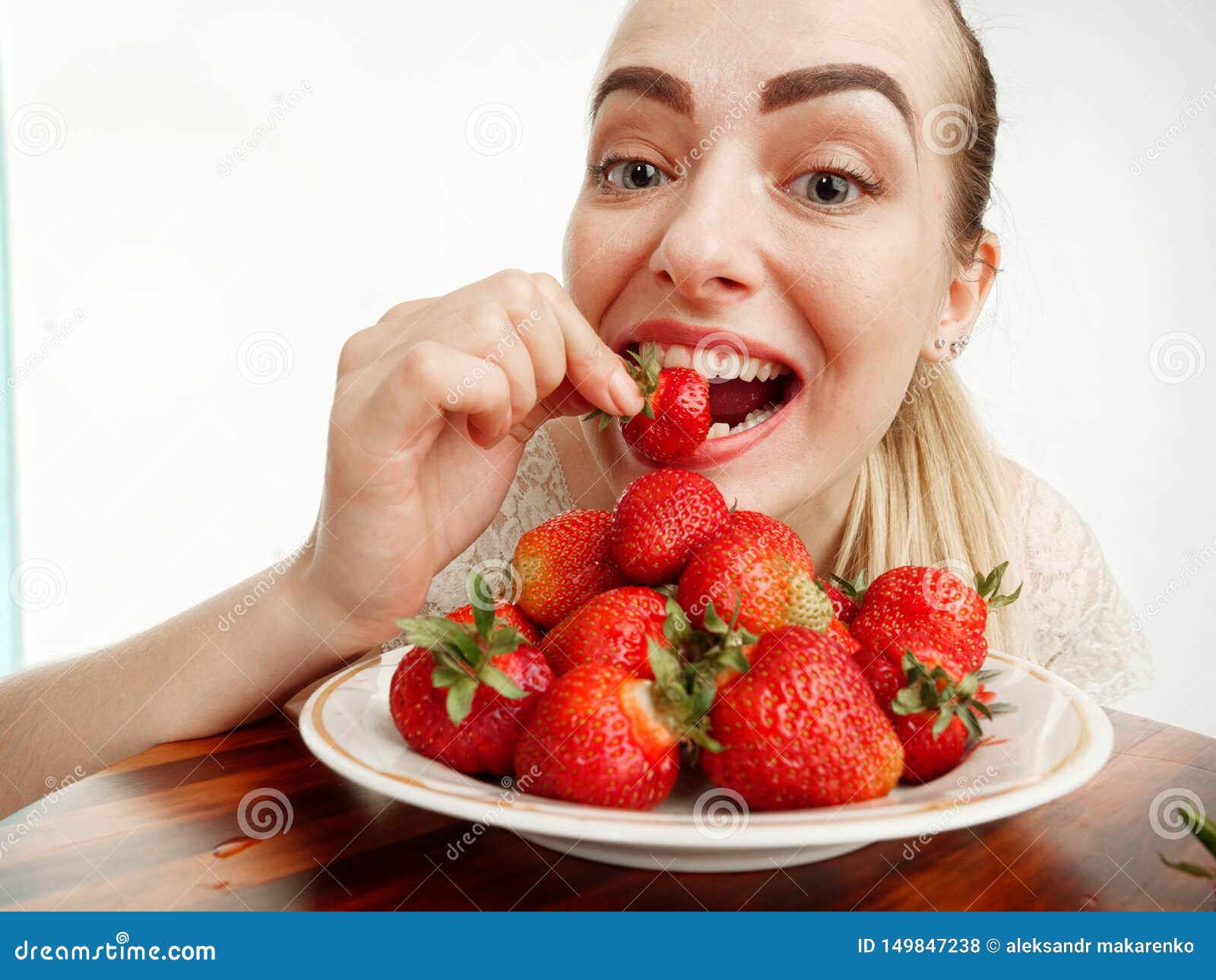 Girl Eagerly Eating Strawberries on White Background Stock Photo