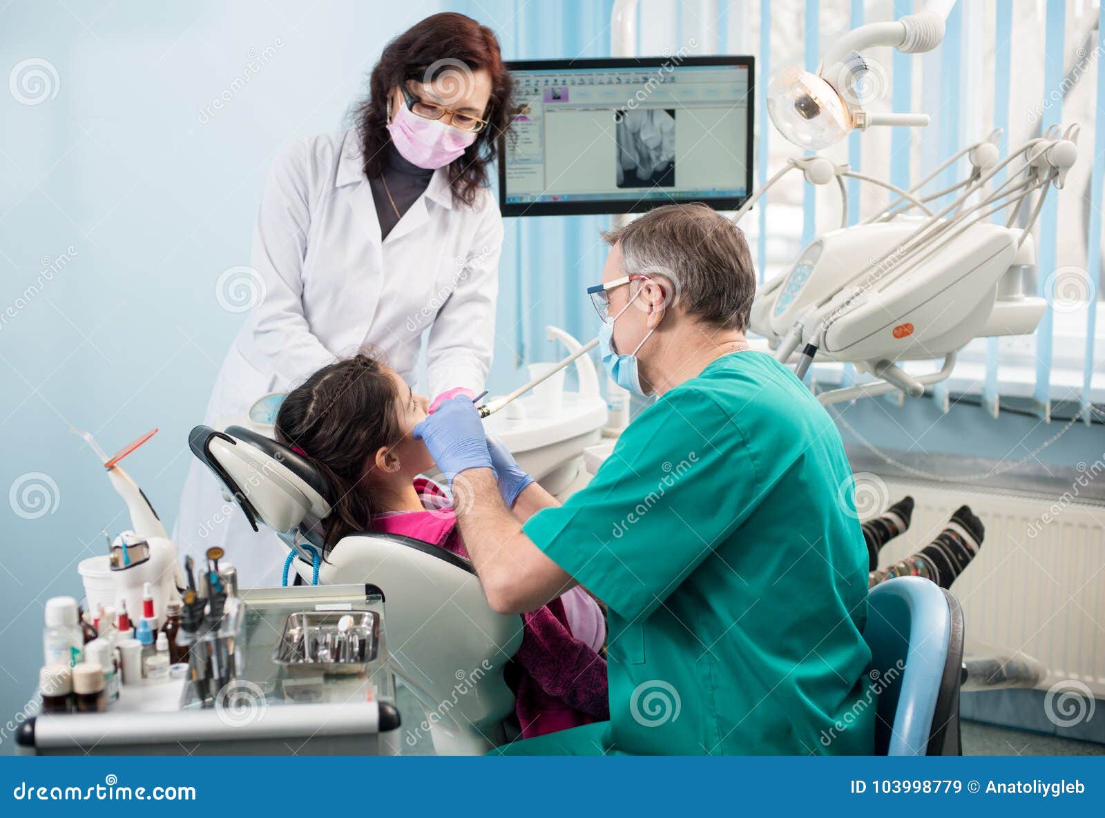 girl with on the first dental visit. senior pediatric dentist with nurse treating patient teeth at the dental office