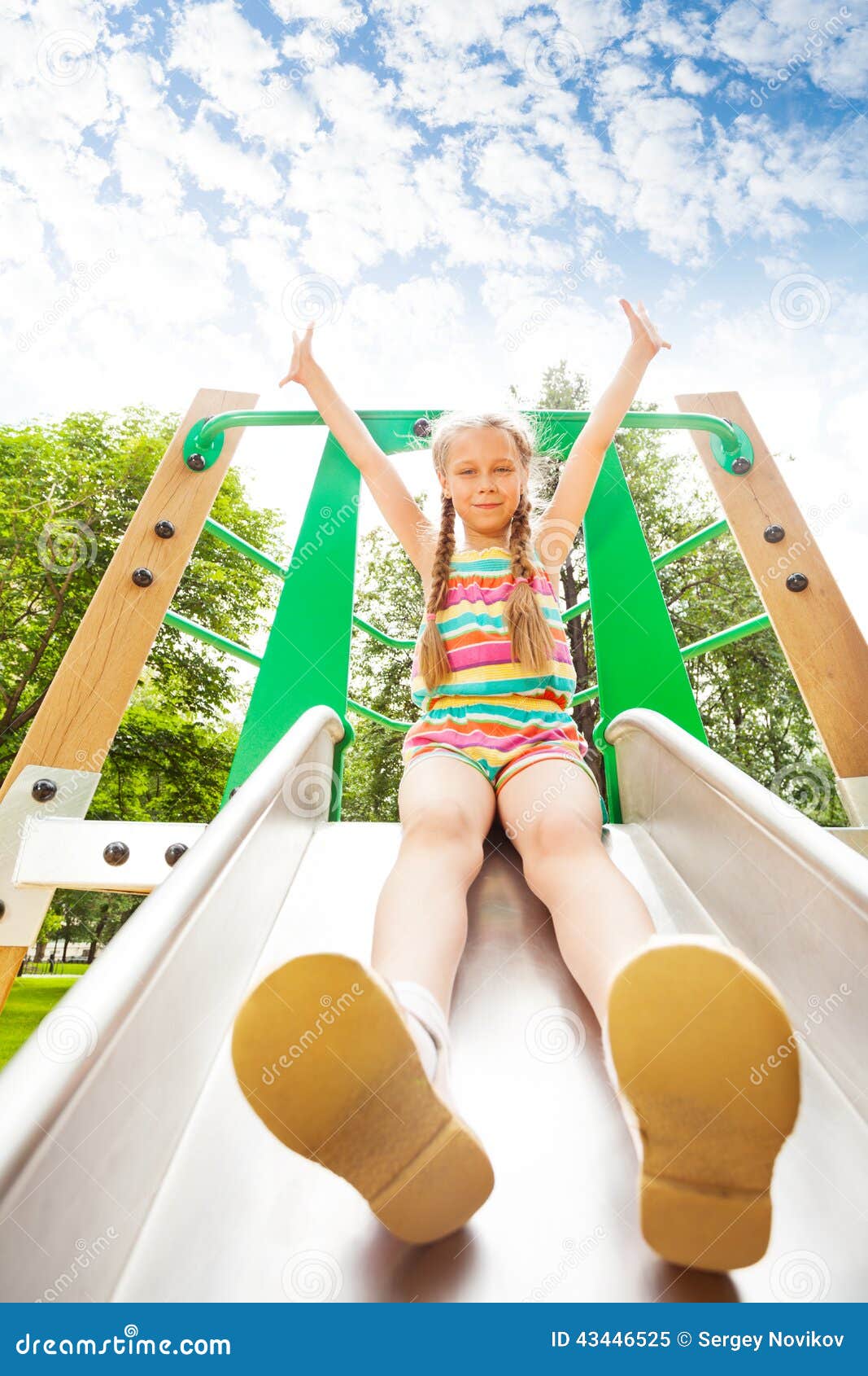 girl with hands up sits on playground chute