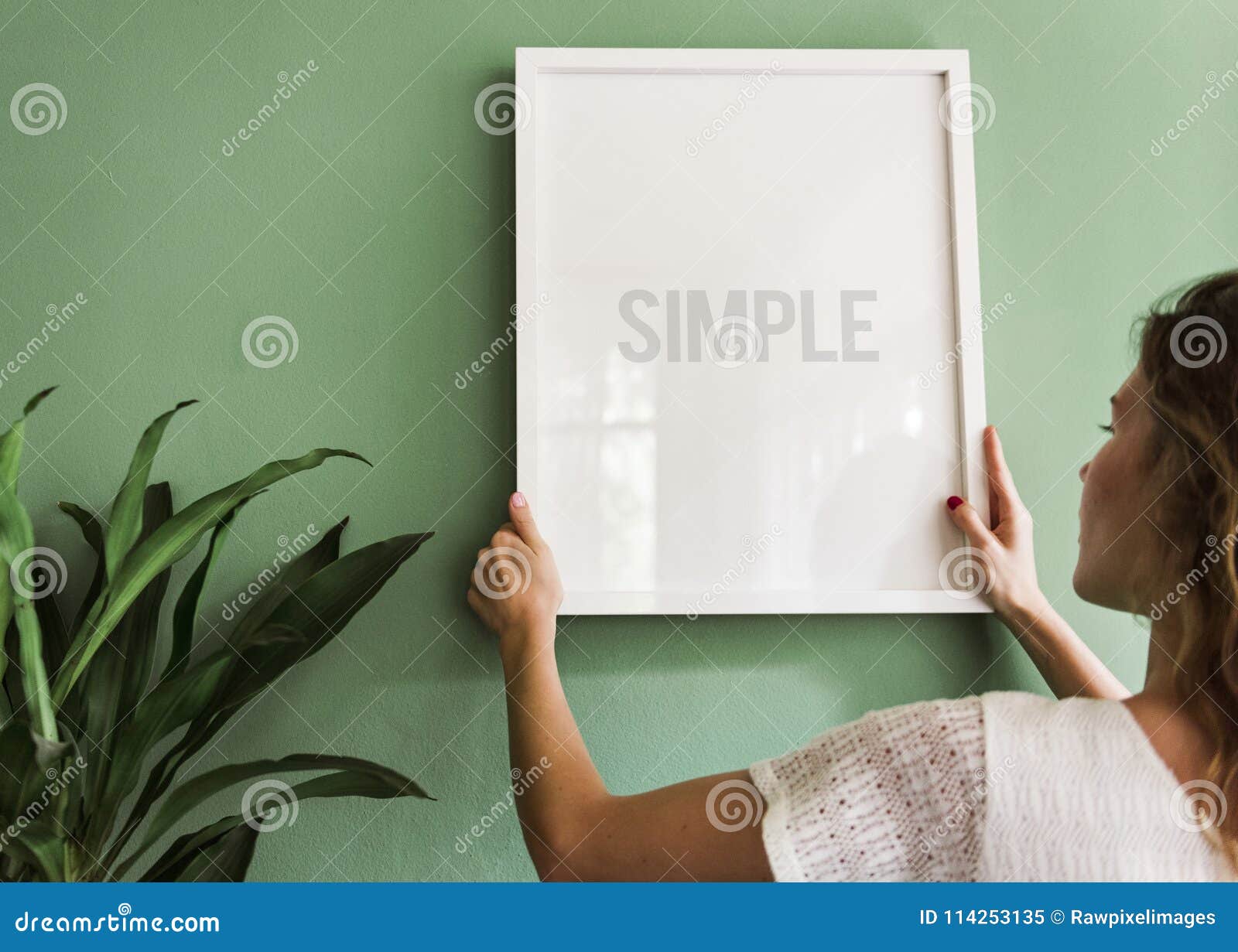 girl hanging a frame on a green wall