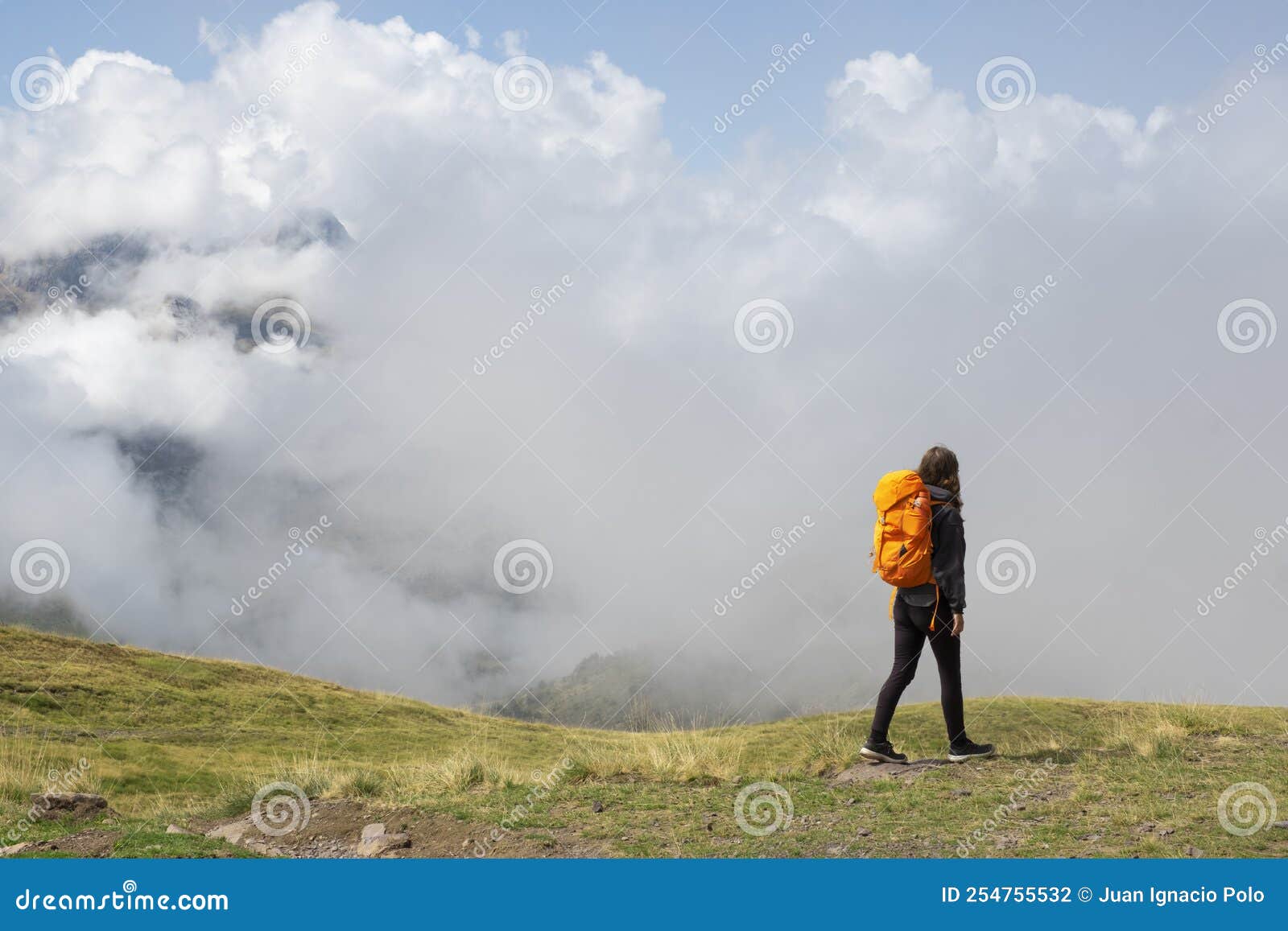 girl hiking in the pyrenees, with the mountains in the clouds in the background