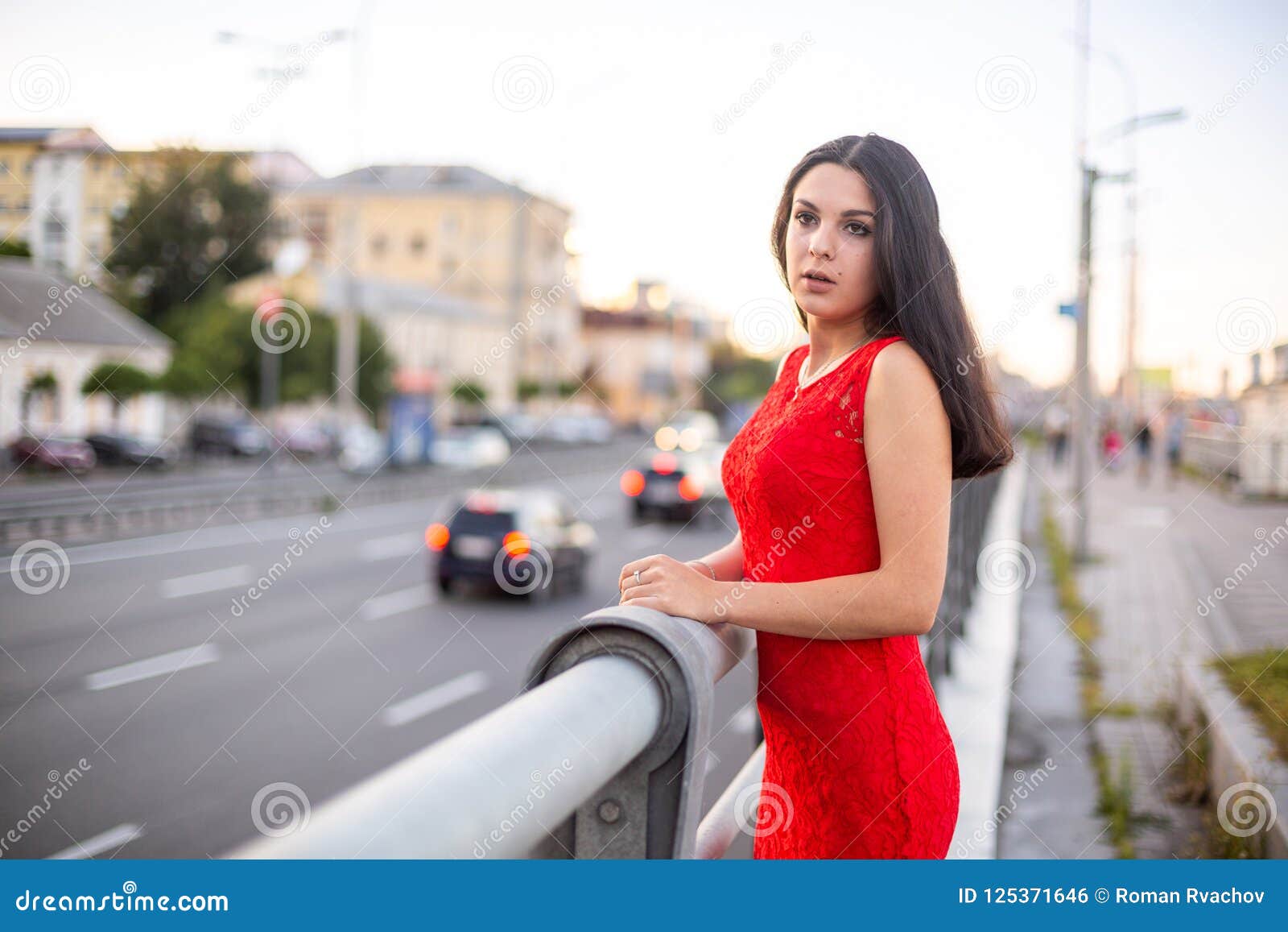 Girl in a Red Dress is Standing Near the Fence of the Roadway. Stock ...