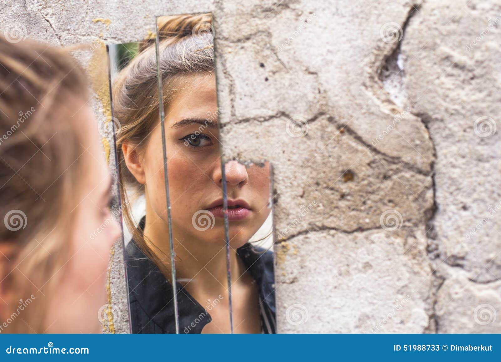 girl looking at her reflection in the mirror fragments on the wall at street.