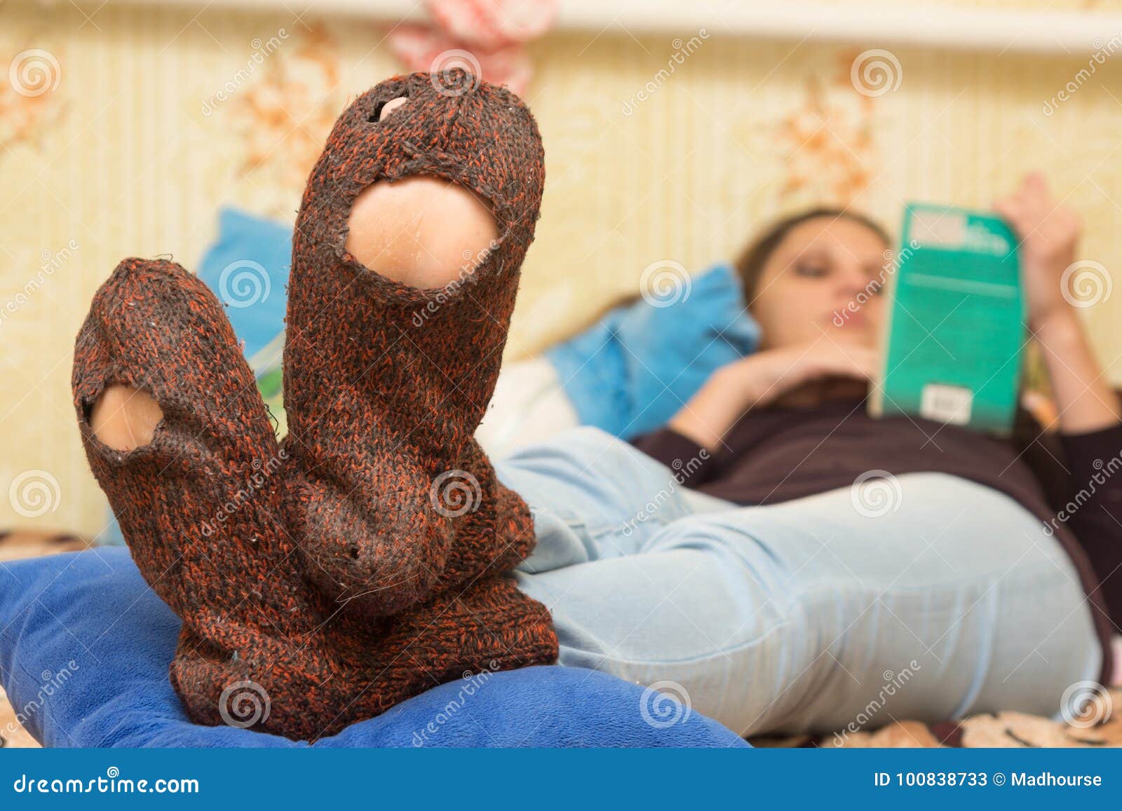 the girl is lying on couch and is reading a book, in the foreground the holey socks