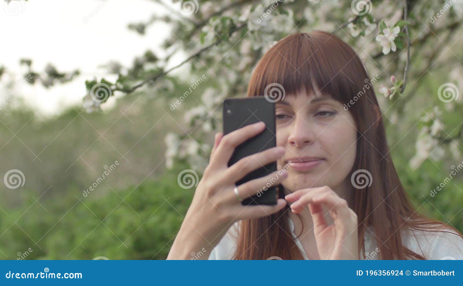 Girl Makes Selfie In The Garden An Attractive Red Haired Woman Smiles Making Selfi Using A