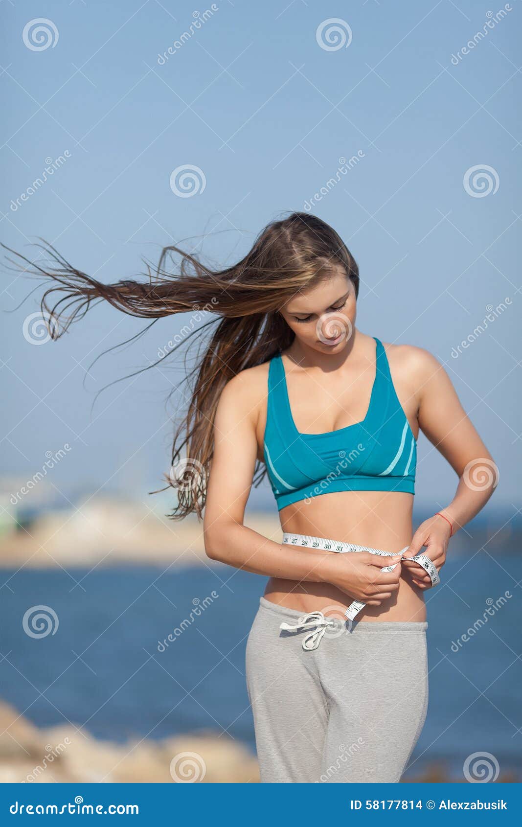 Girl Measures Her Waist Looking Down. Attractive Young Woman In Sports Bra  With Tape Measure On Background Of Sky Stock Photo, Picture and Royalty  Free Image. Image 38922572.