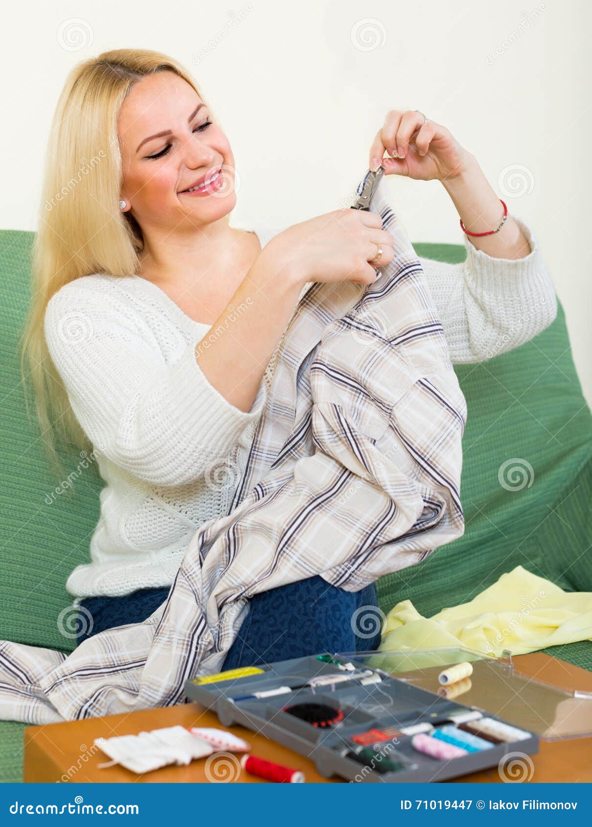 Girl mending linen. Attentive american girl on couch mending linen and smiling