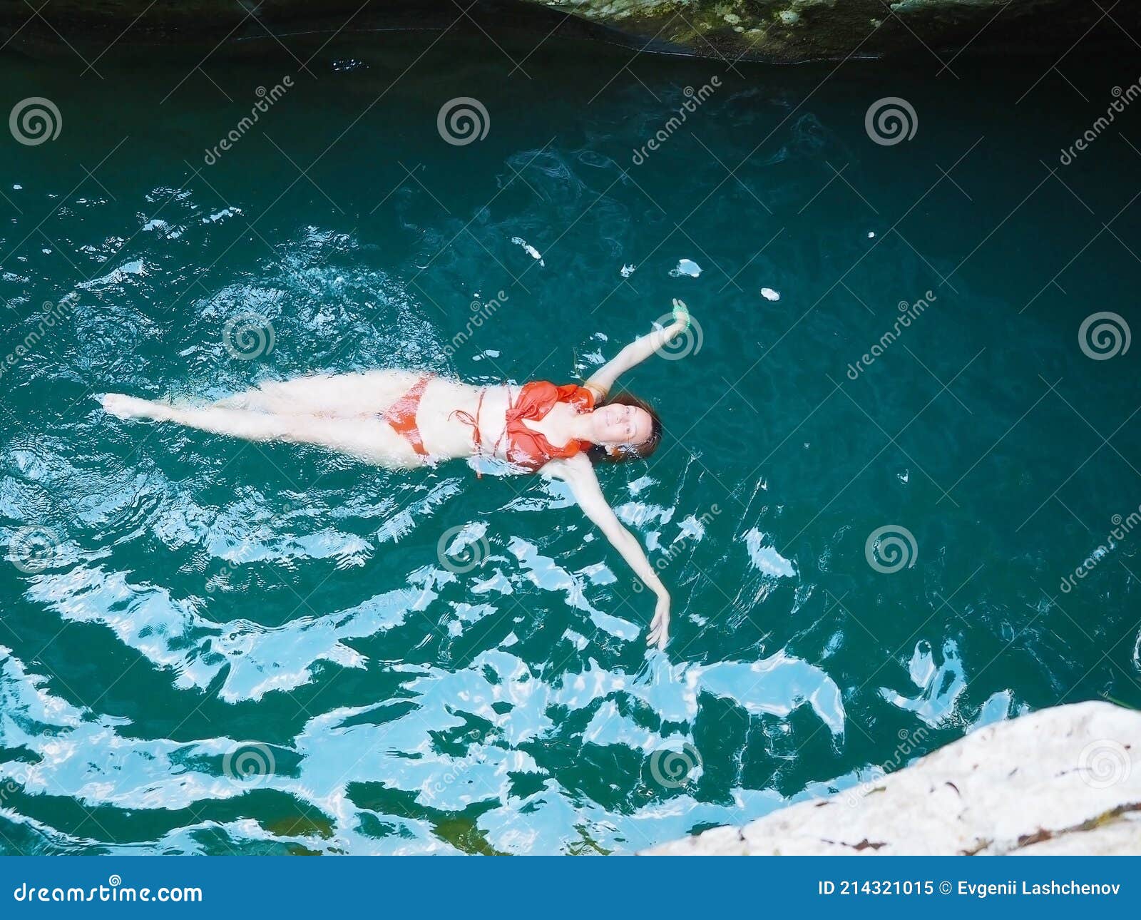 Girl in an Orange Bikini Swims on Her Back in a Turquoise River Stock