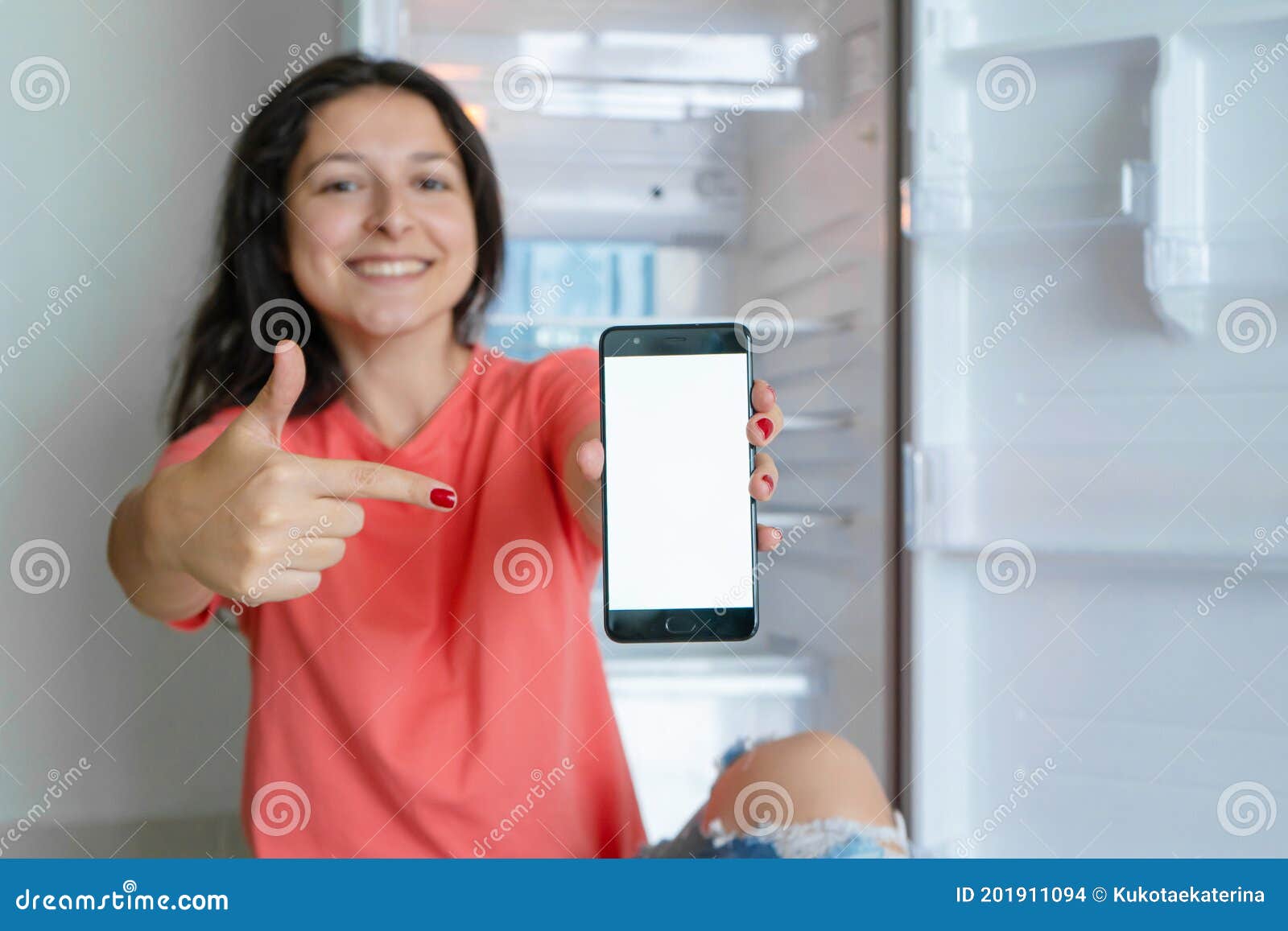 A Girl Orders Food Using a Smartphone. Empty Refrigerator with No Food