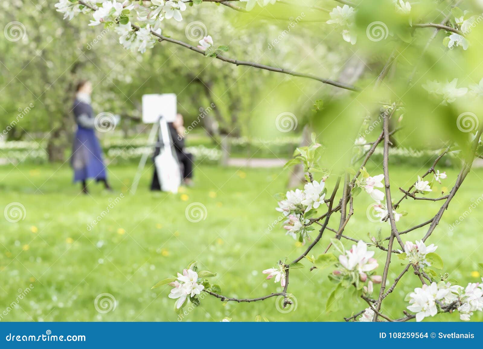 girl paints painting on canvas of easel in park with blooming sakura. blurred image for spring creative background