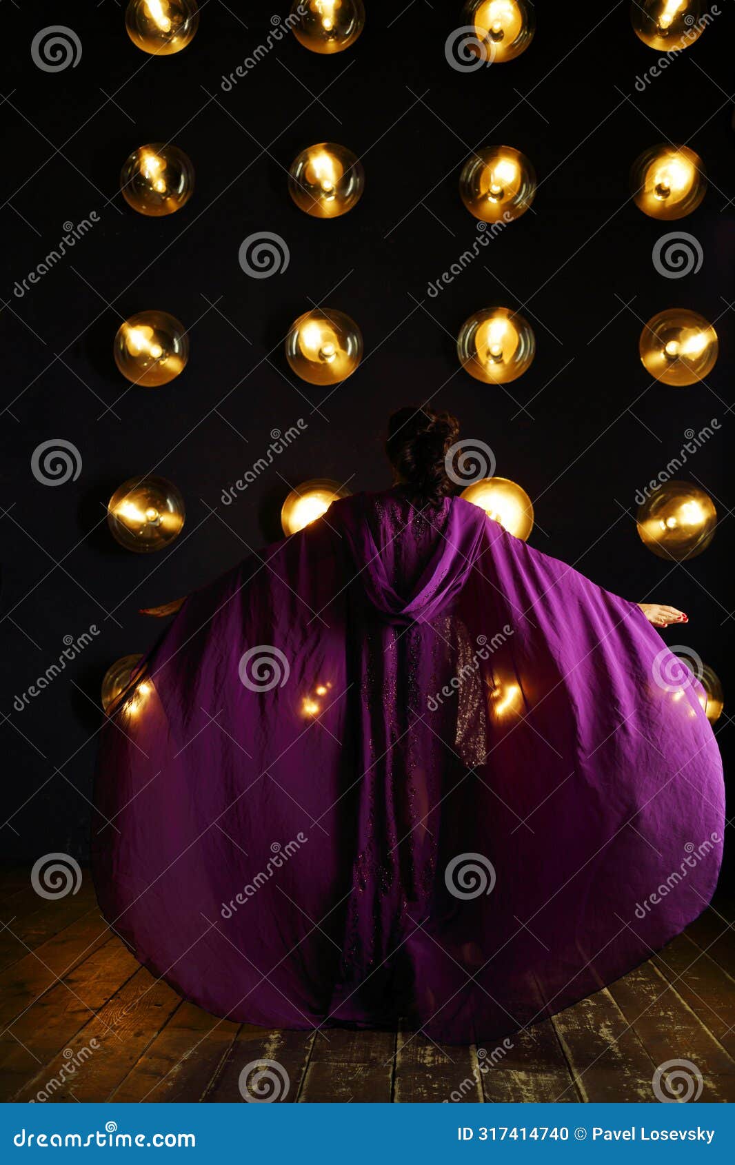 girl in purple mantle poses near wall with lamps