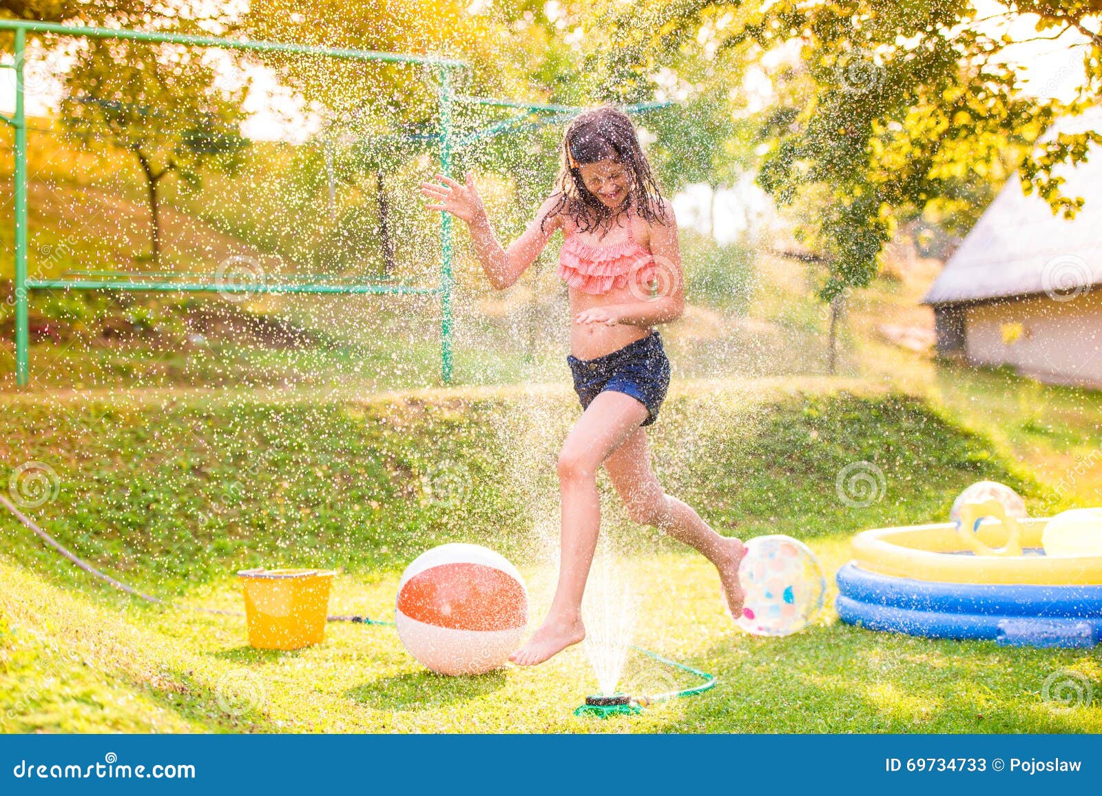 Girl running above a sprinkler, sunny summer back yard 