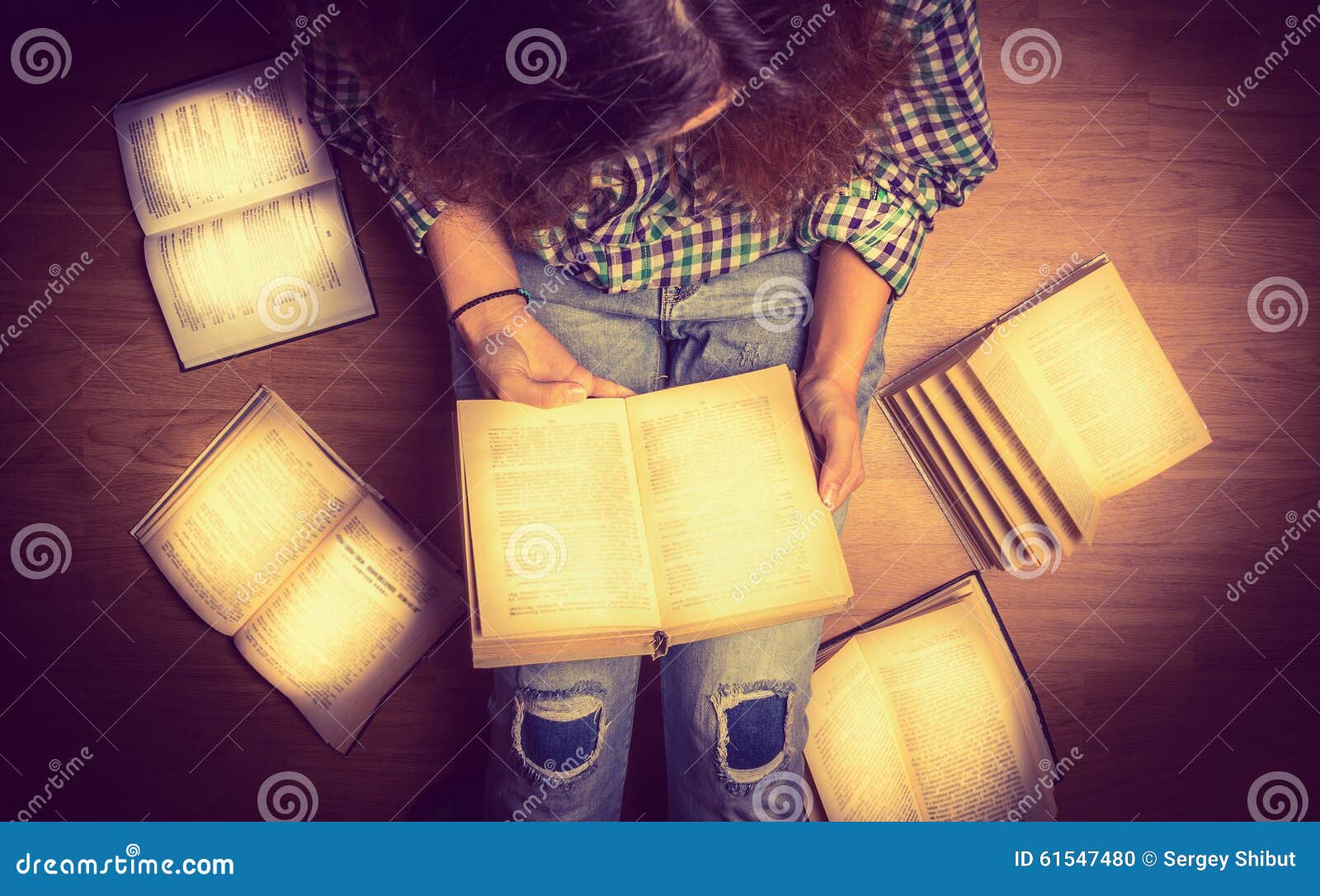 girl in a shirt holding a book sitting on the floor around her spread open books close up retro toning