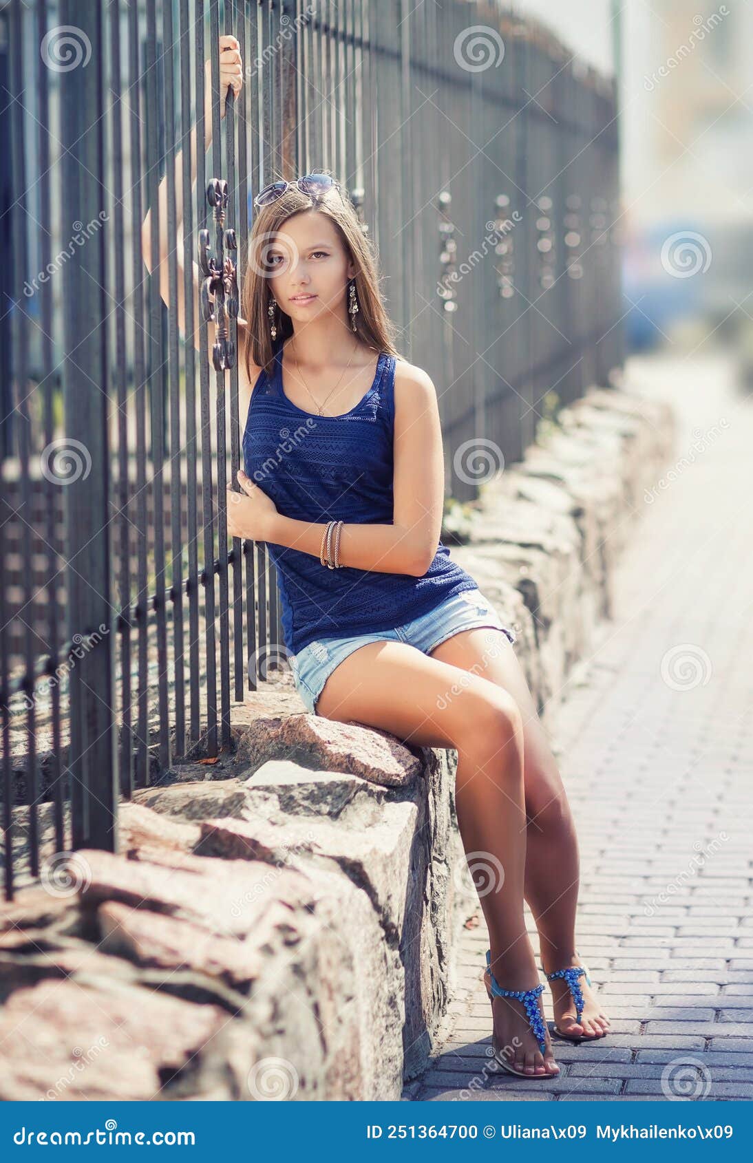 A Girl Sits by the Fence on a Summer Day. she is in the City on the ...