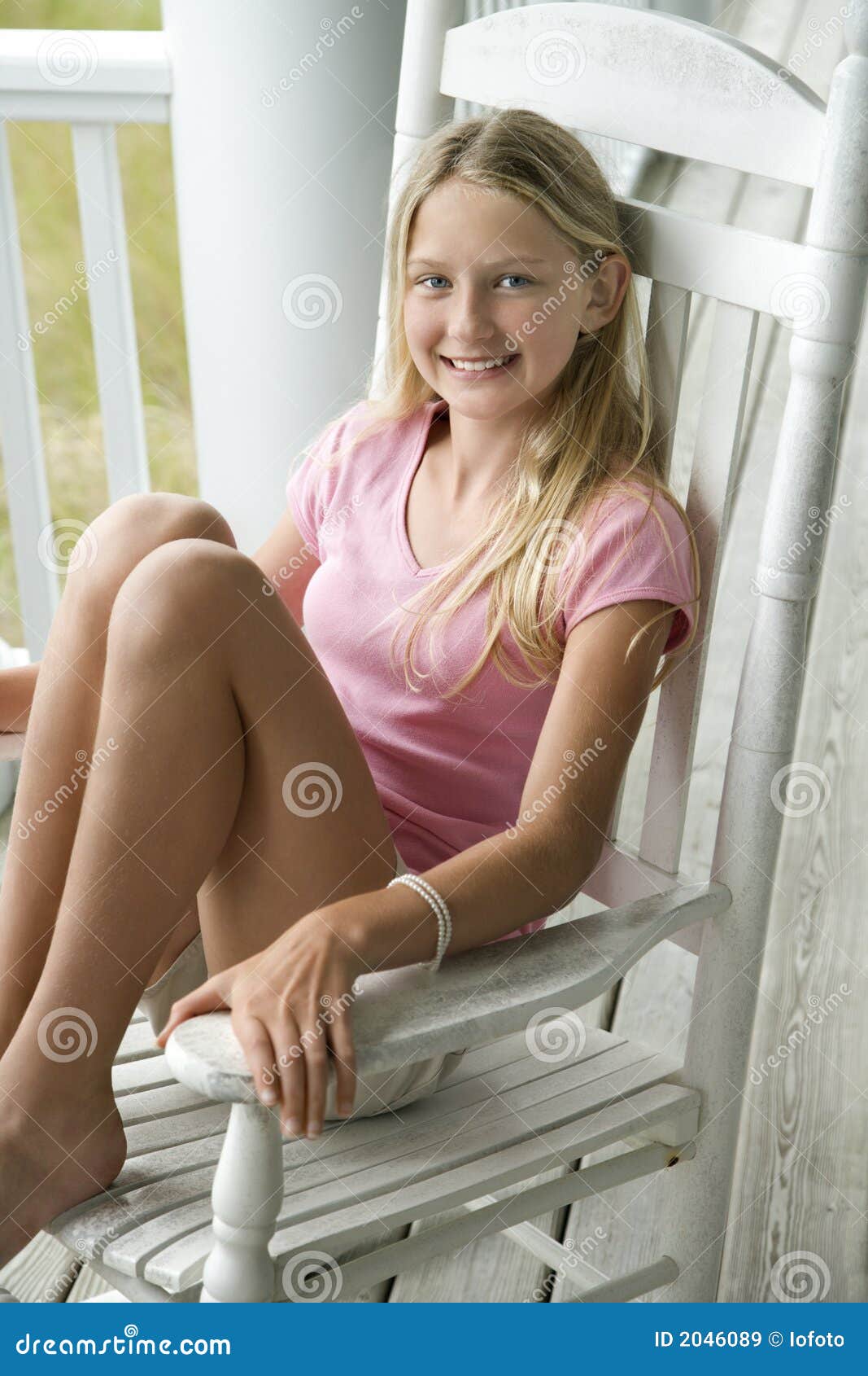 Caucasian pre-teen girl sitting in rocking chair on porch smiling.