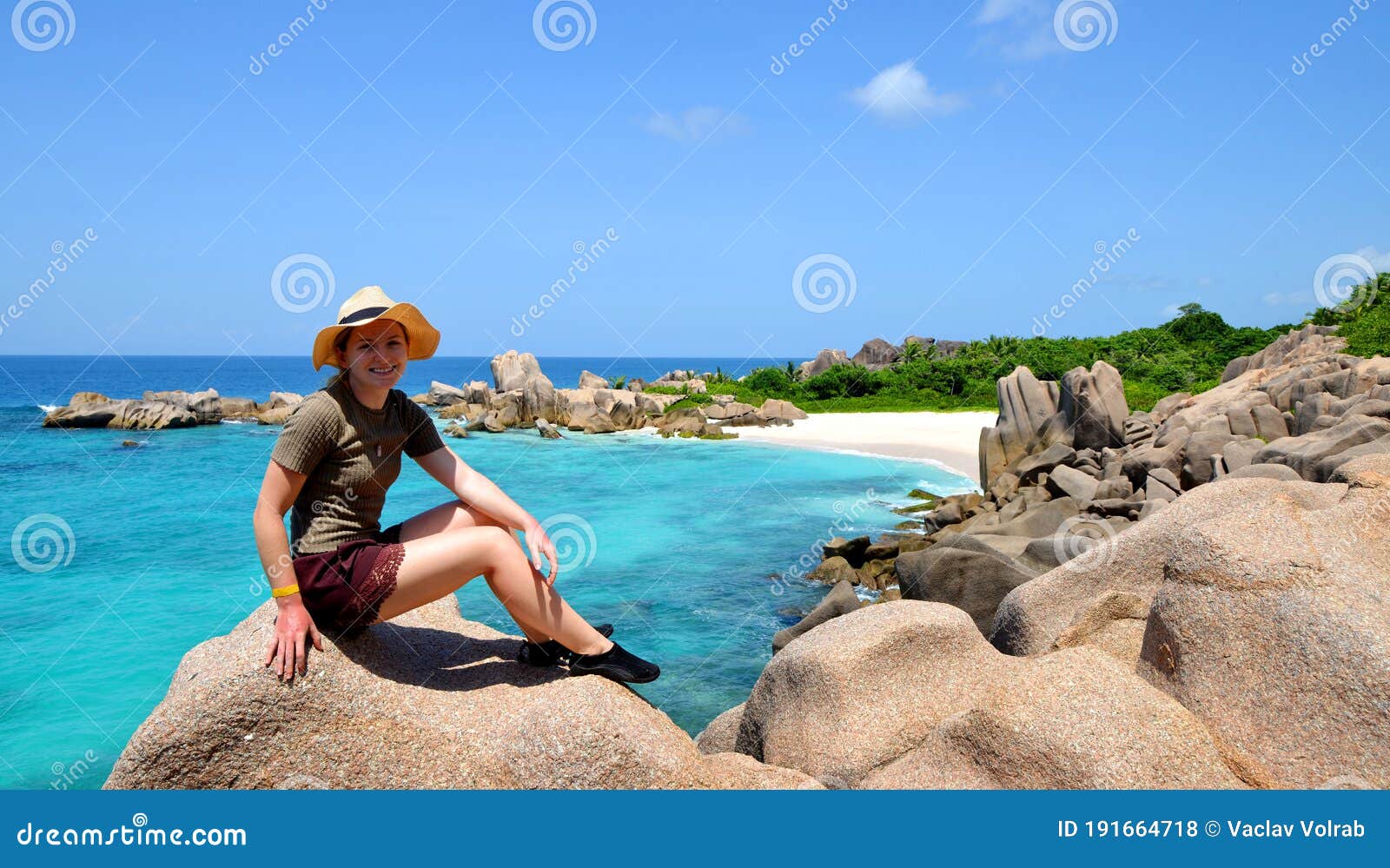 girl sitting on granite stone near anse marron beach, la digue island, indian ocean, seychelles.
