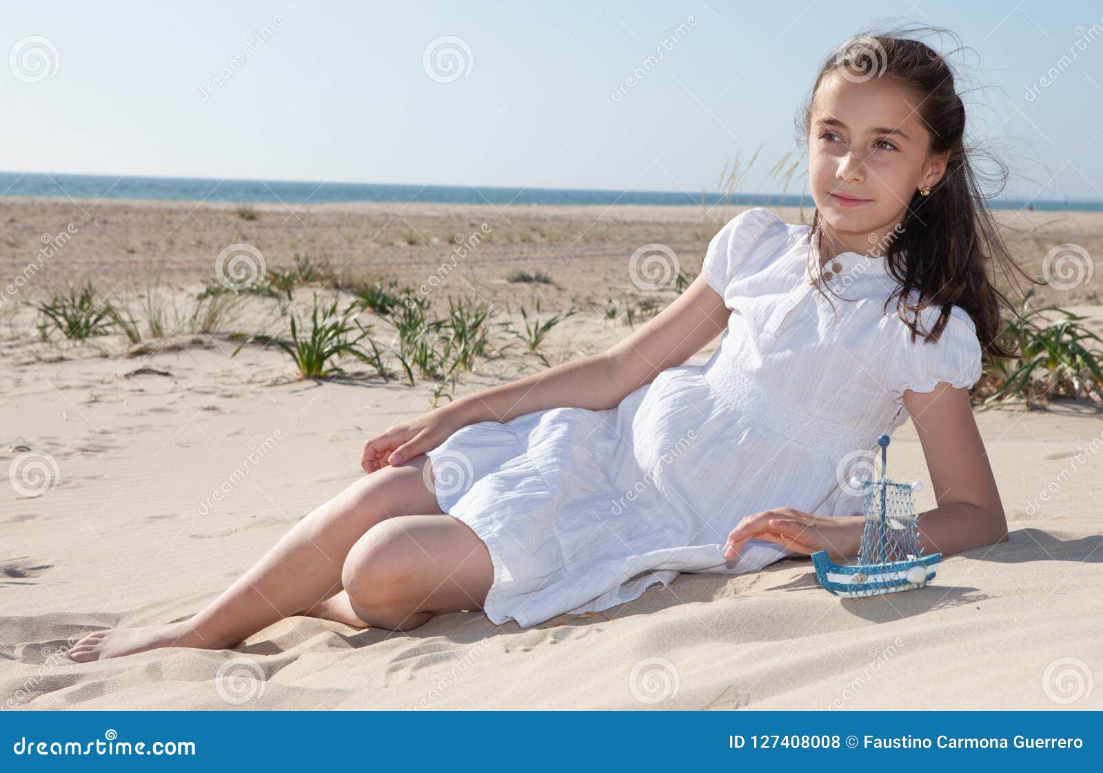 Girl Sitting on the Sand on the Beach in a White Dress Stock Photo