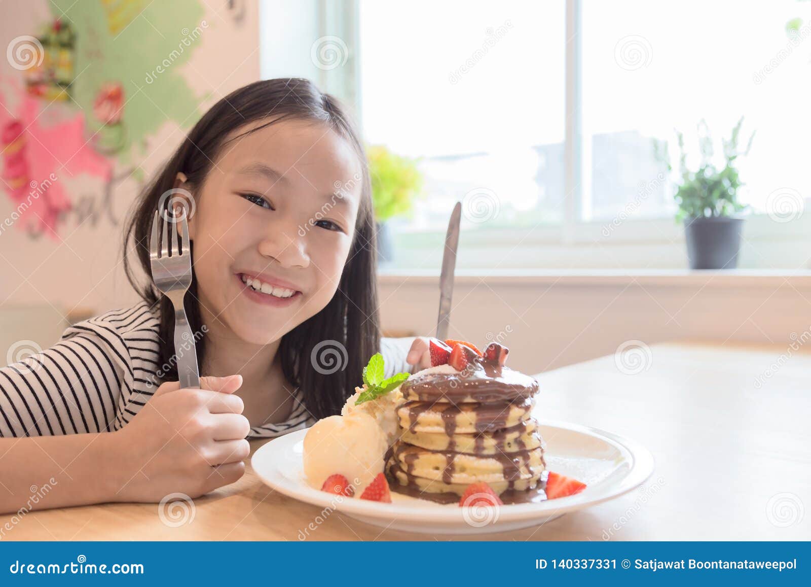 girl is smiling happily,holding a knife and fork is preparing to eat pancakes in restaurants