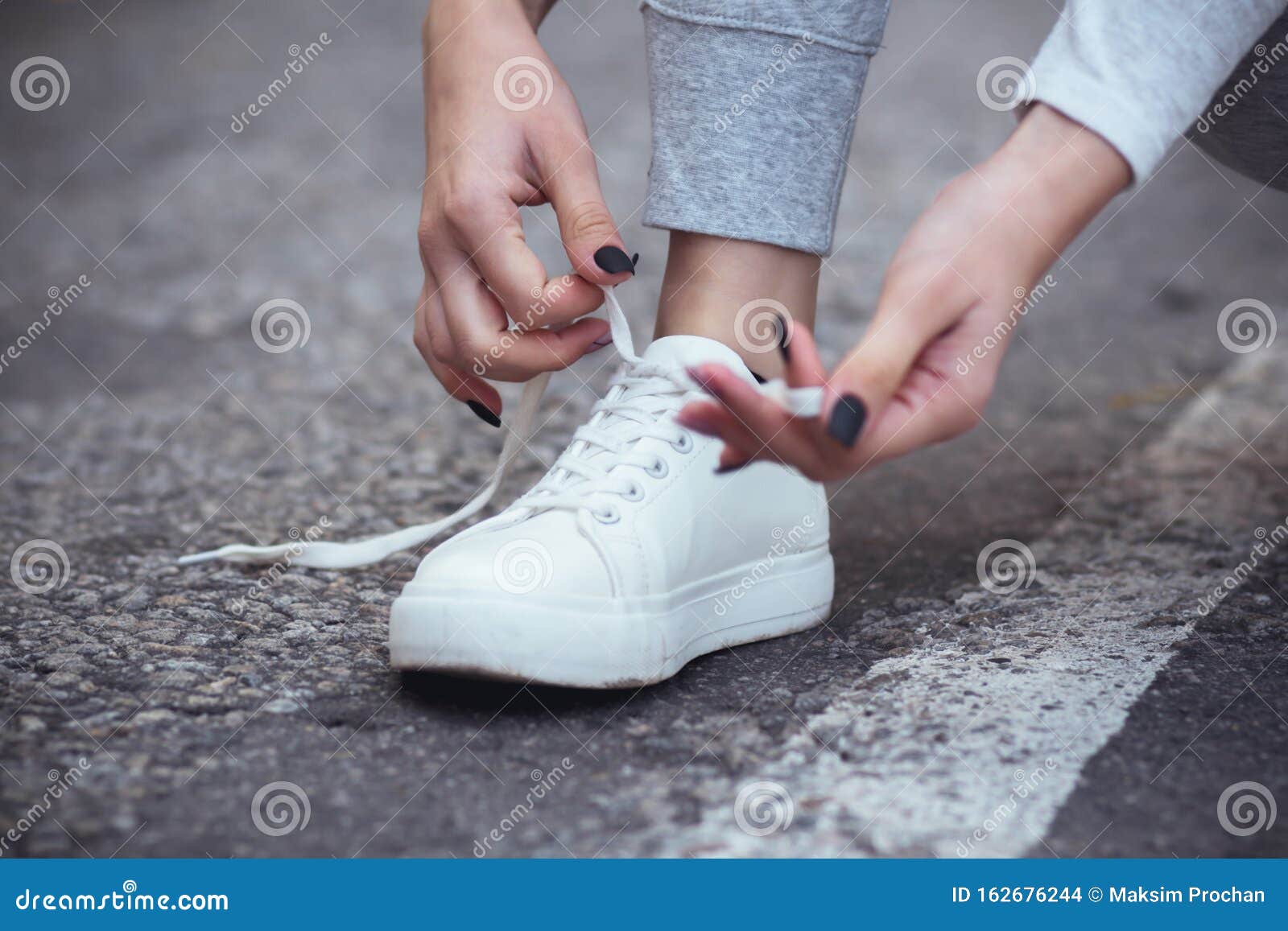 Girl Squatted Down To Tie Shoelaces on White Sneakers on Asphalt Road ...