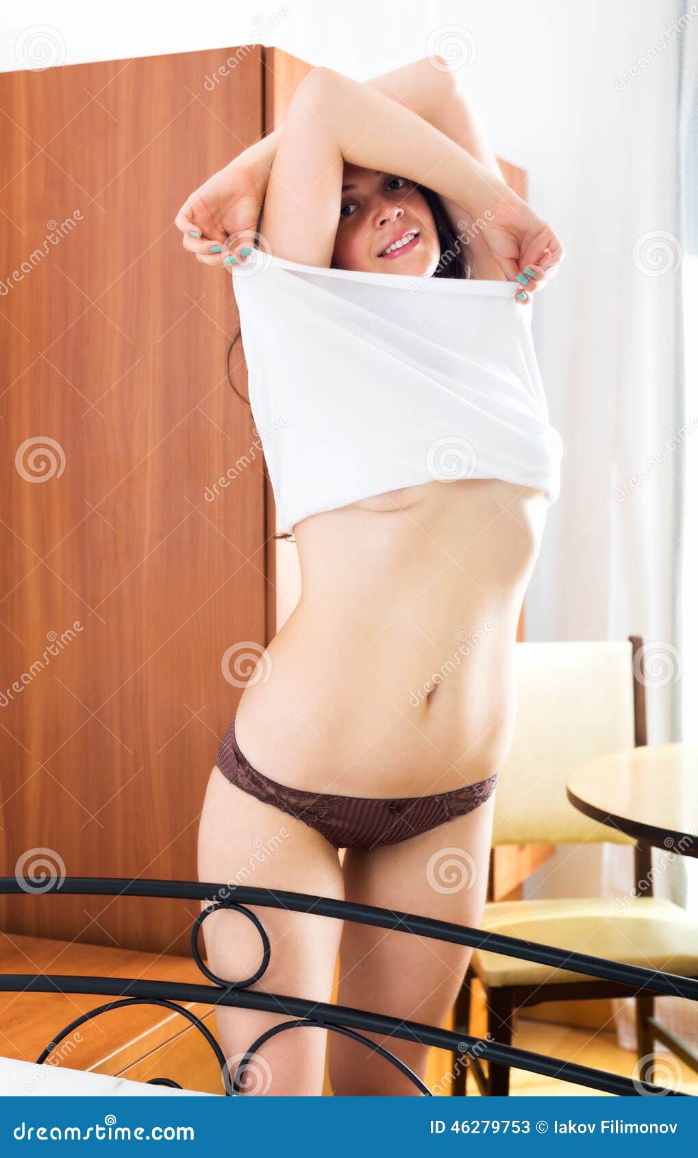 Smiling girl takes off his underwear in bedroom.