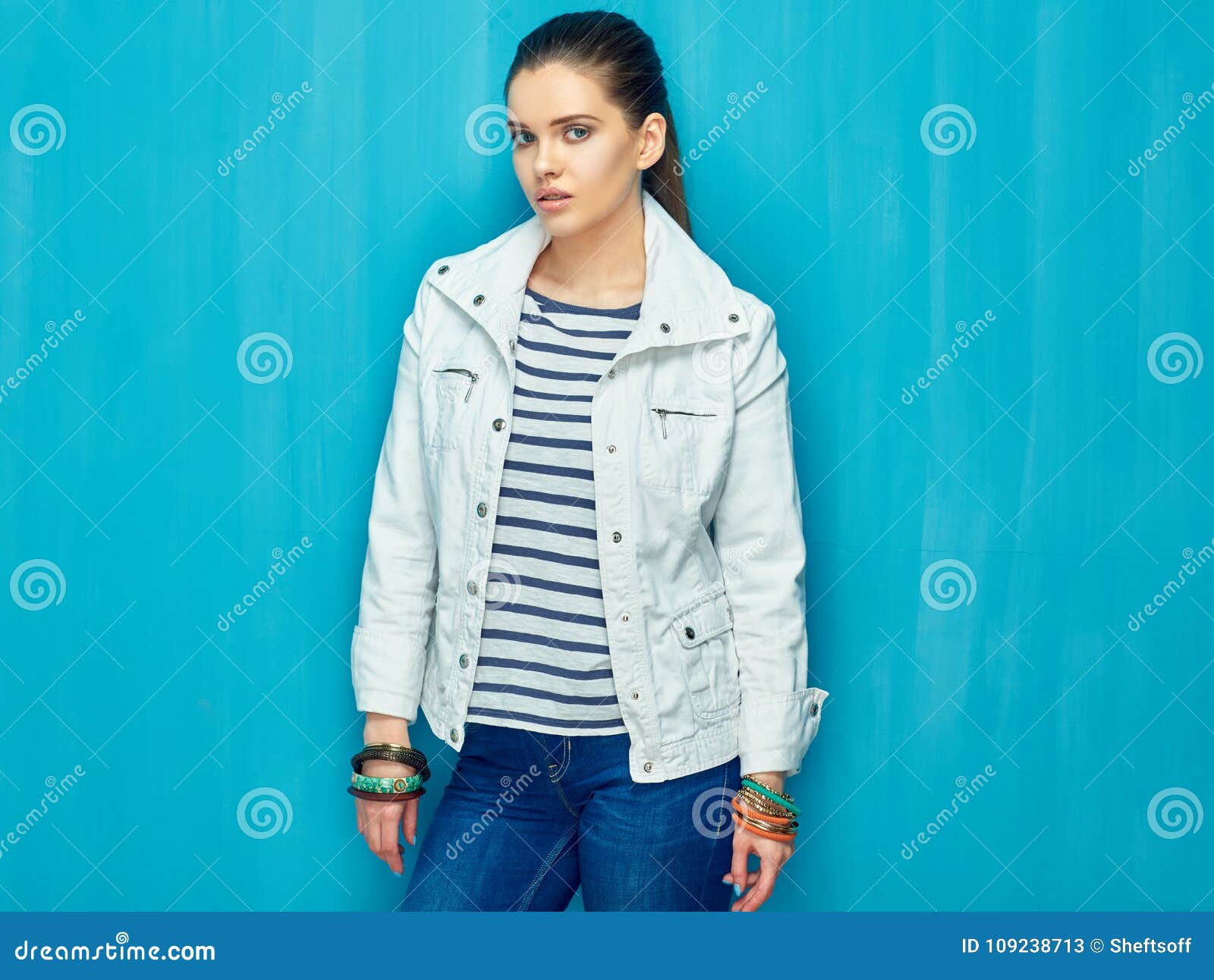 Girl in teen style with long hair standing against blue wall back. Studio fashion portrait.