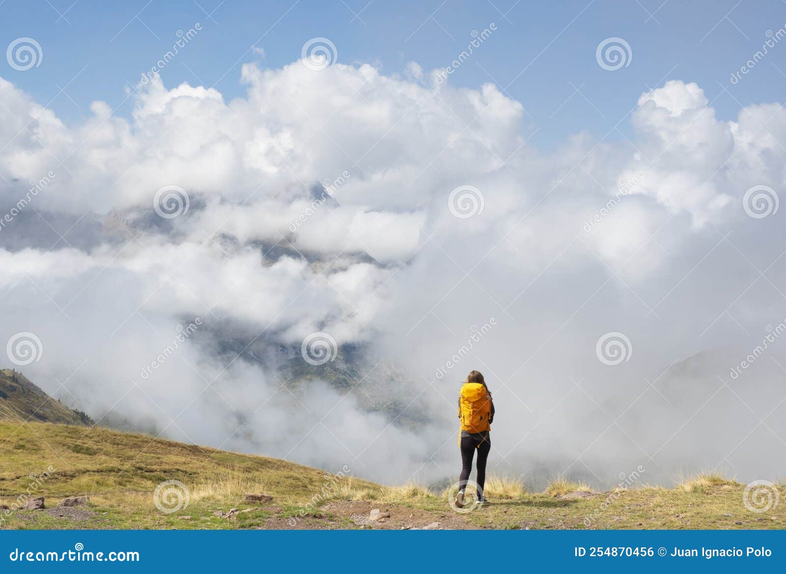 girl with yellow backpack hiking in the pyrenees, with the mountains in the clouds in the background