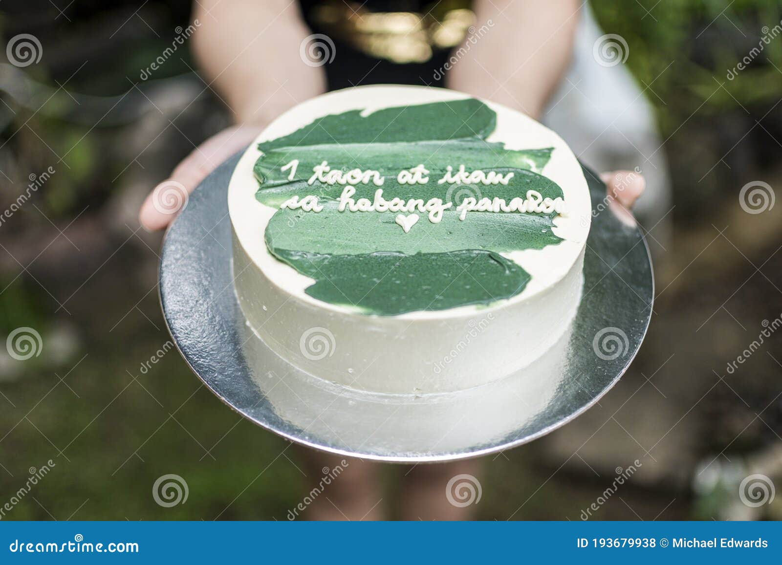 girlfriend handing over a small cake with green icing and a heartwarming message. tagalog words translated as 1 year and forever.
