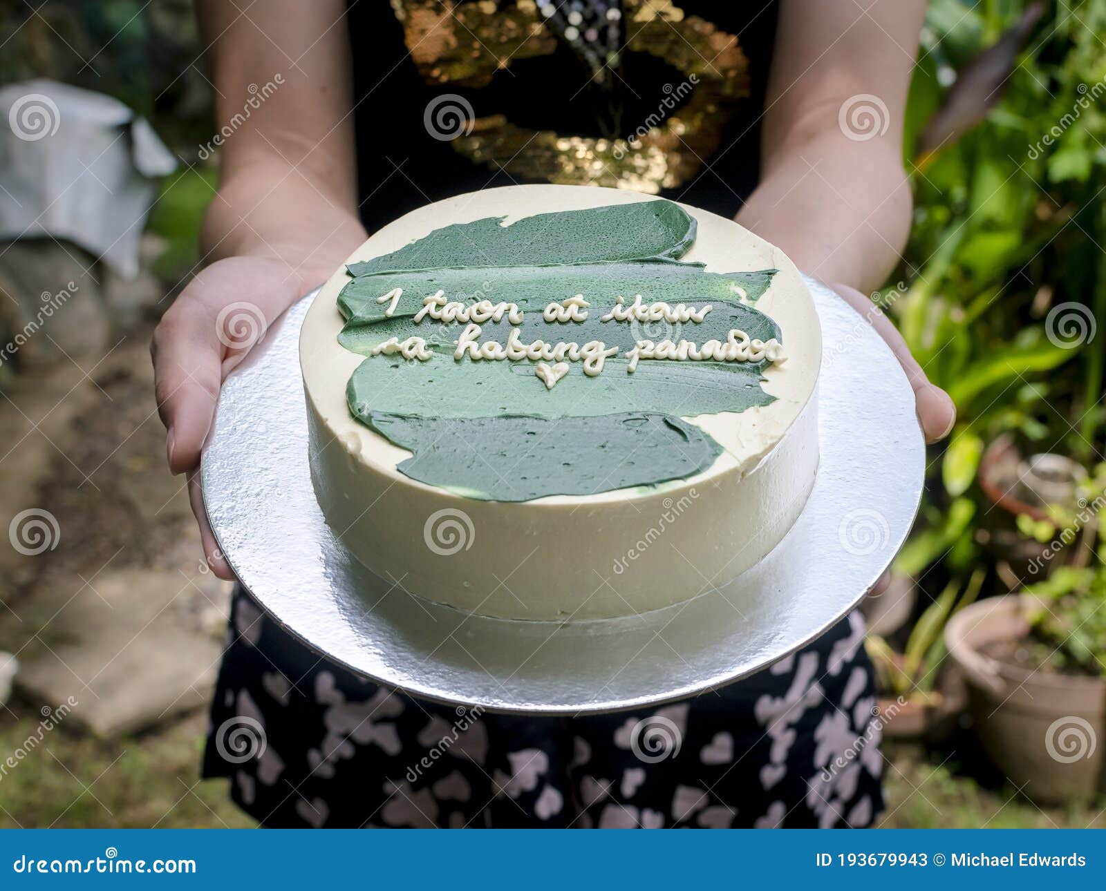 girlfriend handing over a small cake with green icing and a heartwarming message. tagalog words translated as 1 year and forever.