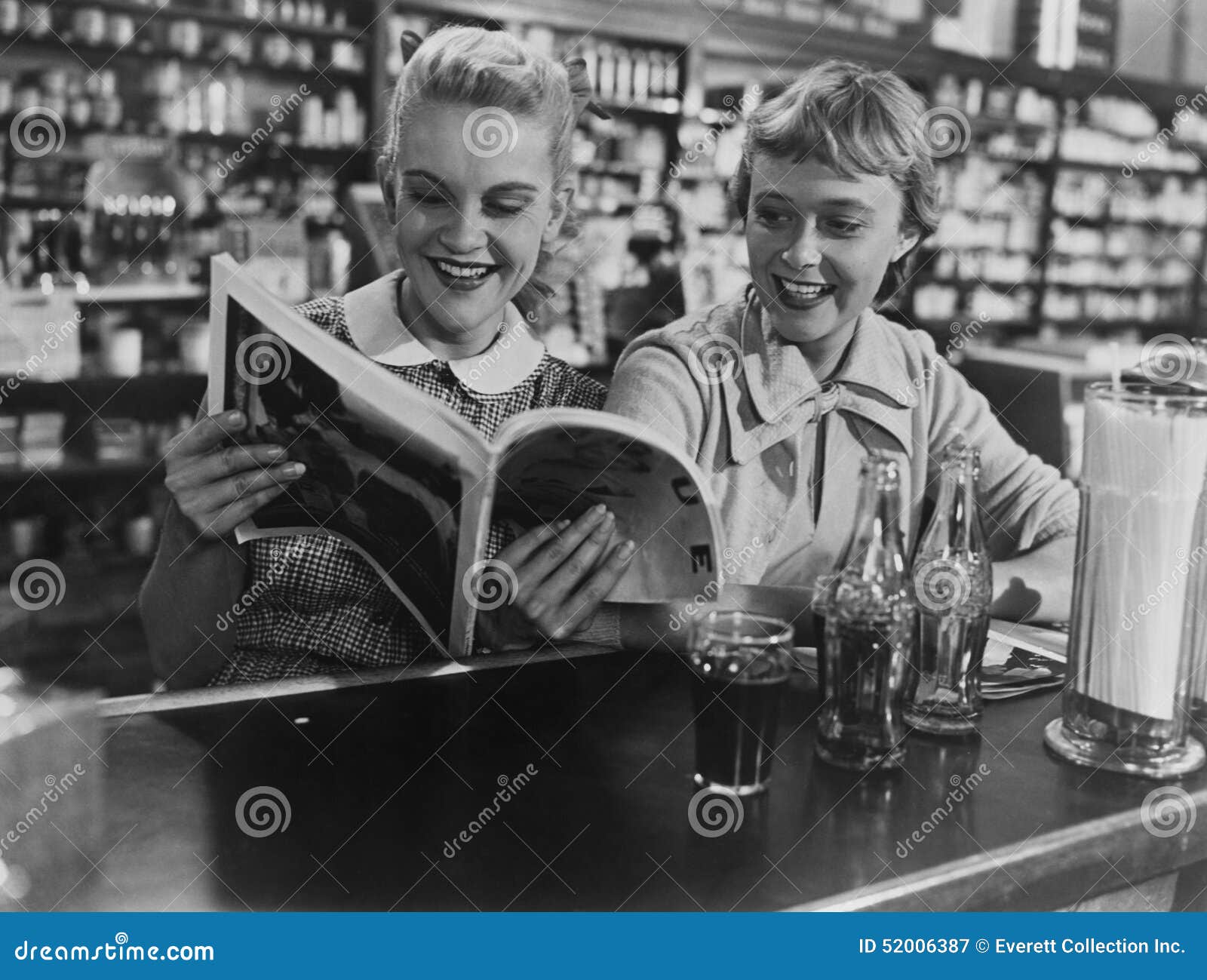 girlfriends looking at magazine at soda fountain