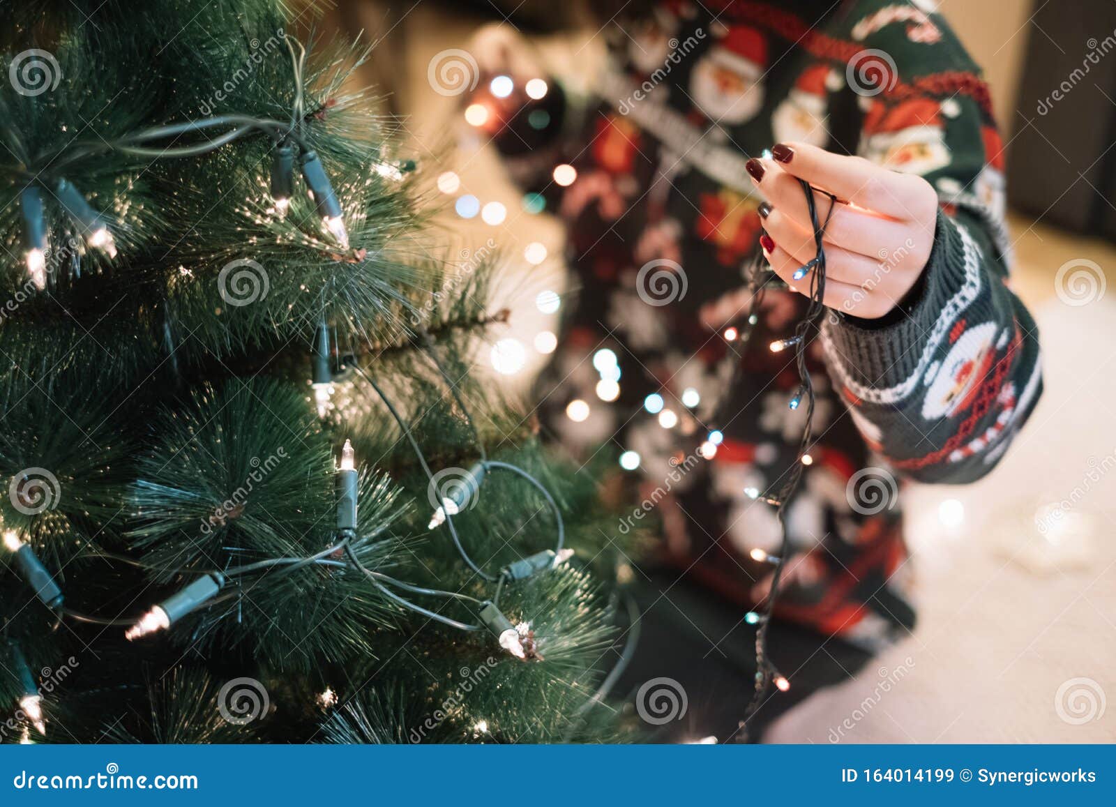 girls hand putting christmas lights to tree
