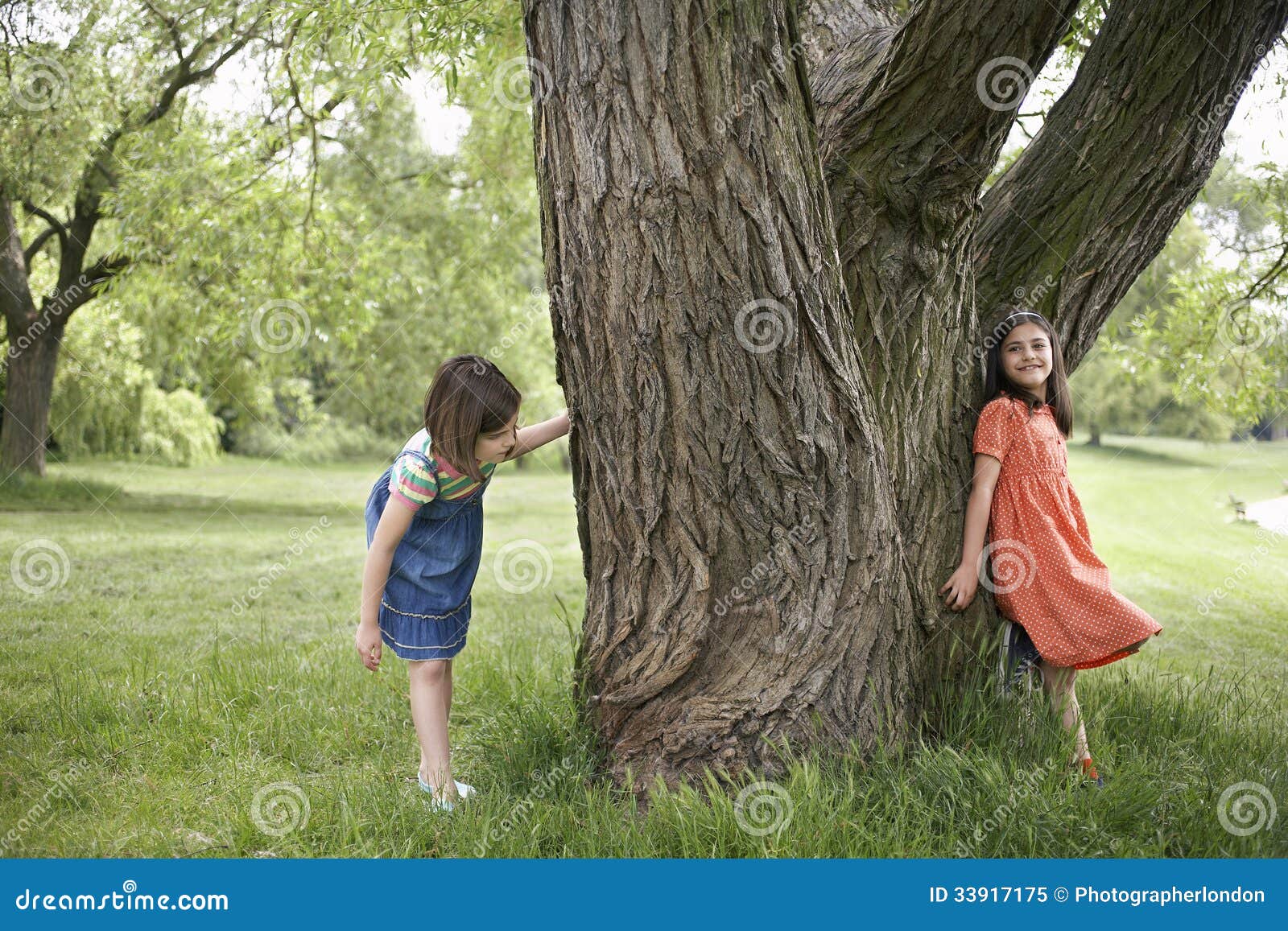 girls playing hide and seek by tree