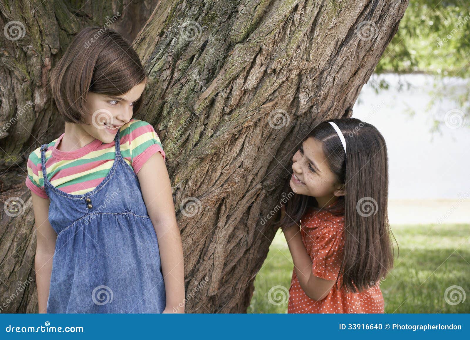 girls playing hide and seek by tree