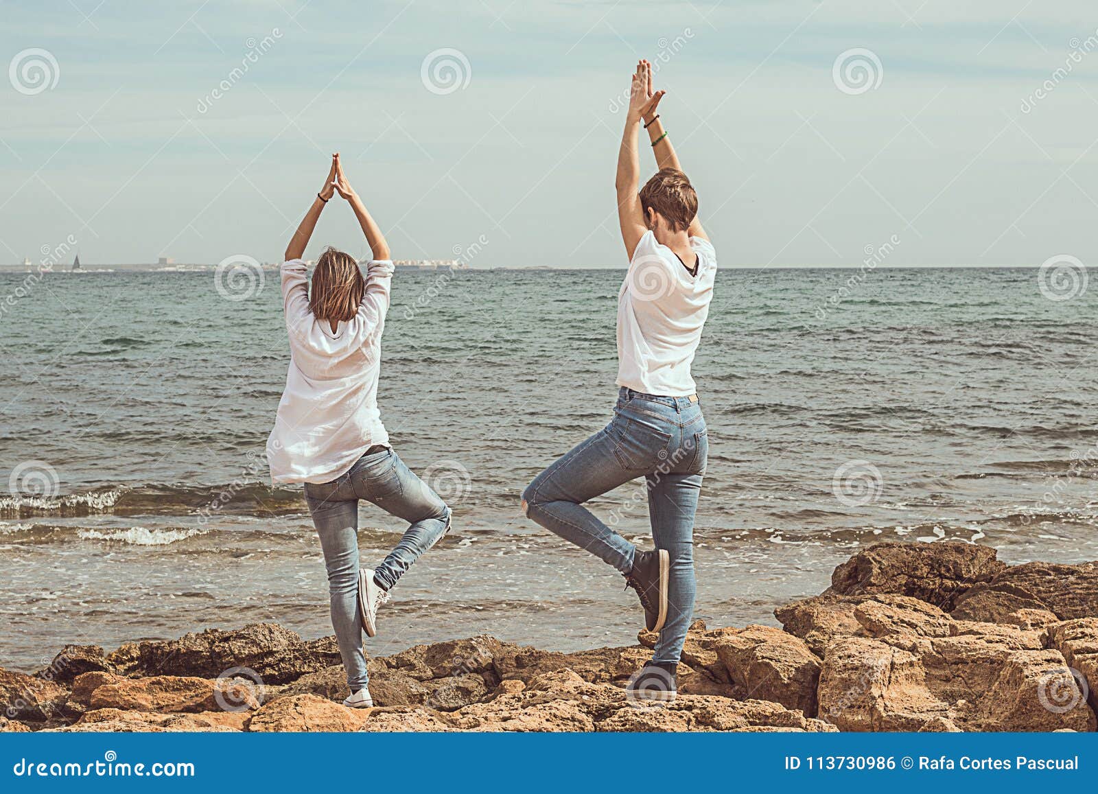 Woman sea yoga. Two happy women practicing yoga on the beach with ocean and  rock mountains. Motivation and inspirational fit and exercising. Healthy  lifestyle outdoors in nature, fitness concept. by panophotograph Vectors