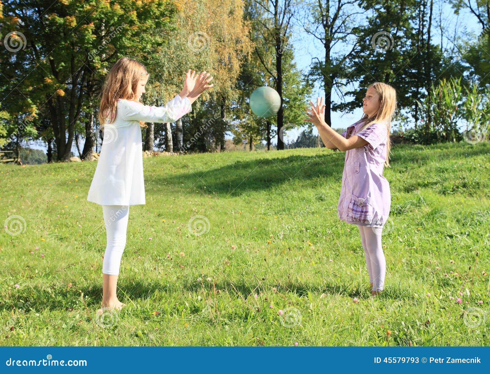 Little barefoot girls throwing a ball on meadow