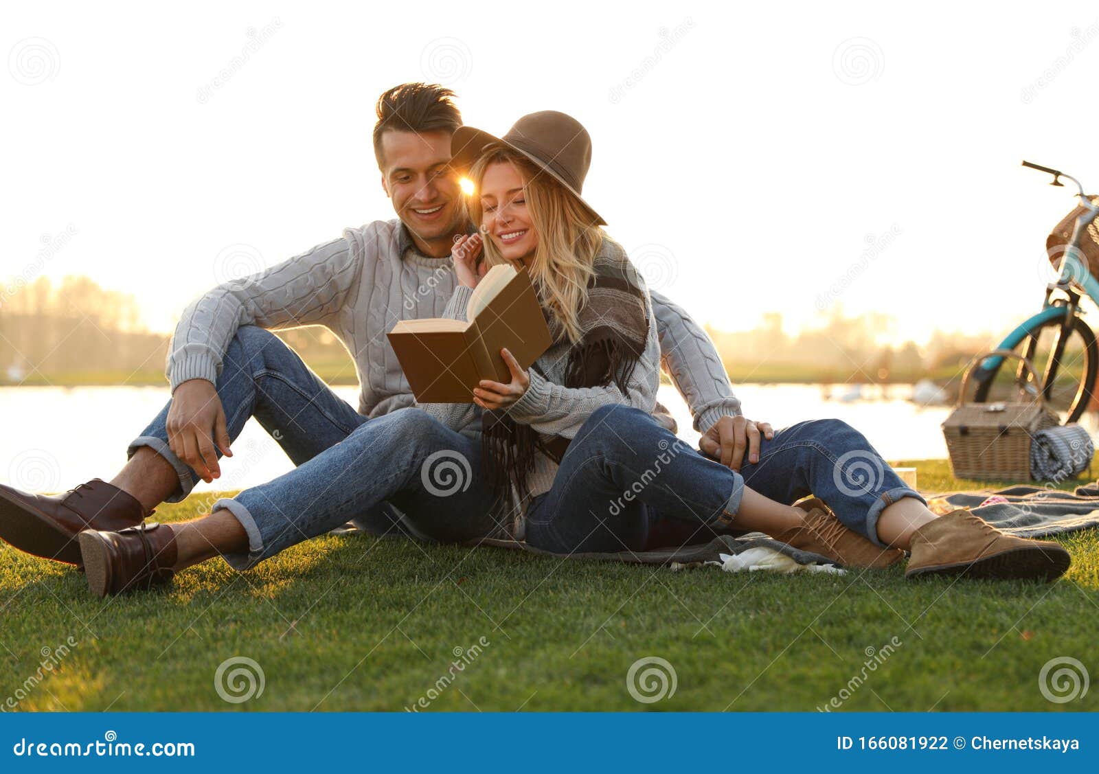 Glad ung läsbok med ett picknick. Gott och gott par som läser boken samtidigt som de har picknick utomhus