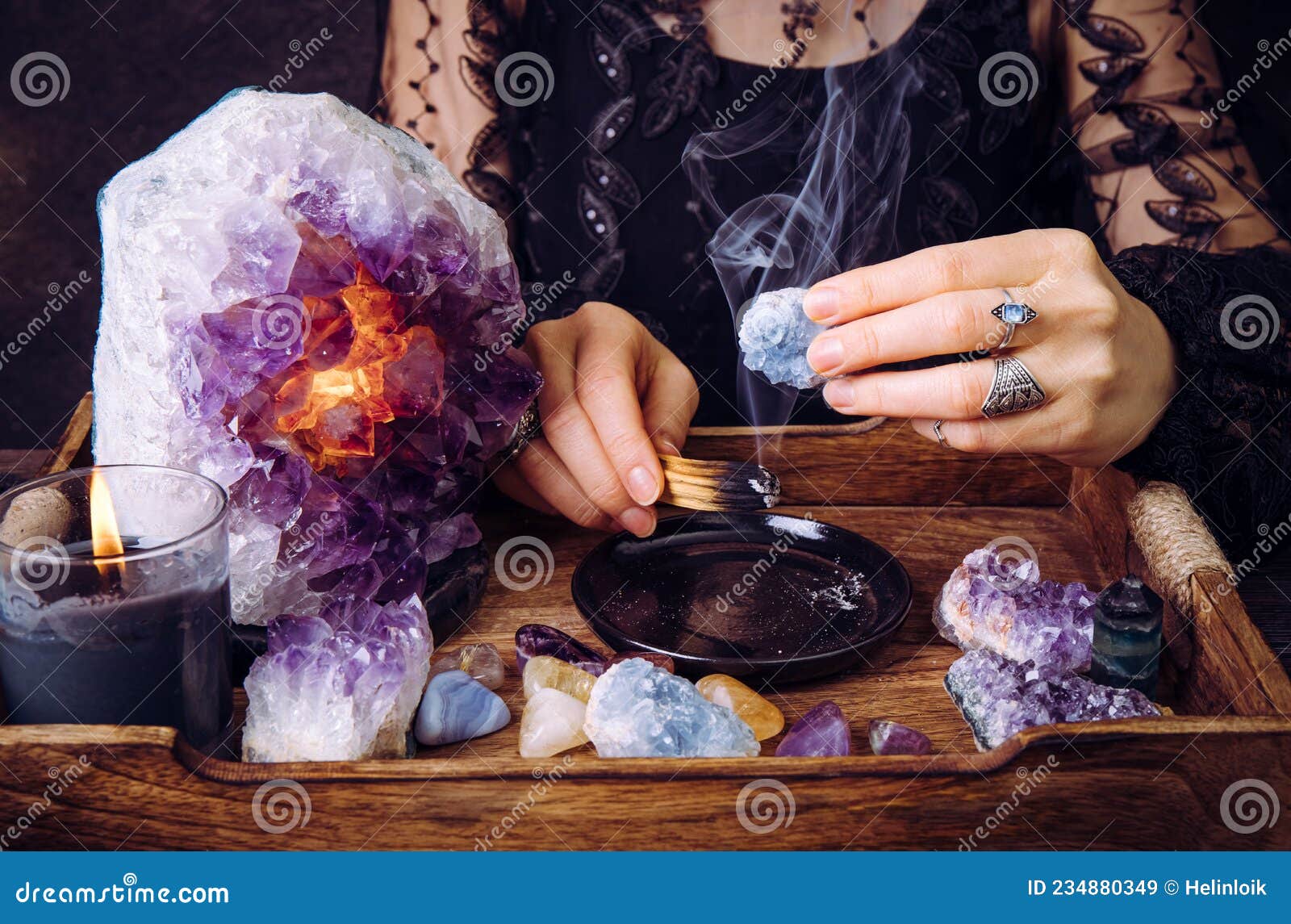 glamorous woman in black dress cleansing crystals gemstones by smudging palo santo wood stick.