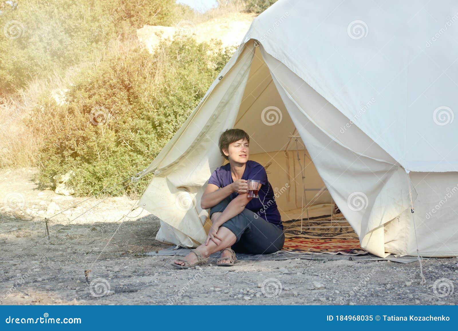 glamping outdoor vacation. woman drinking tea near big camping tent with cozy interior. luxury travel accomodation into the forest
