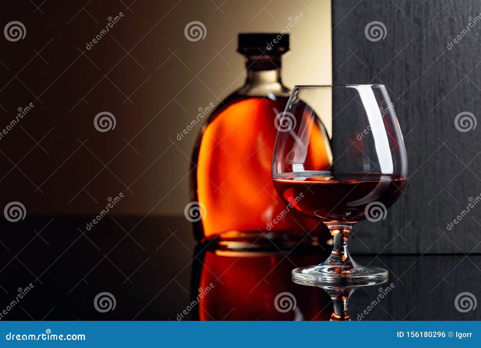 glass and bottle of brandy on a black reflective background