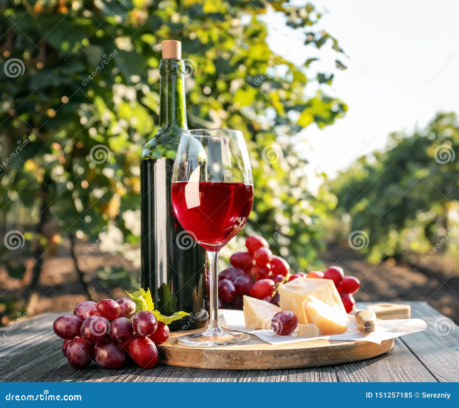 Glass and Bottle of Red Wine with Cheese on Table in Vineyard Stock