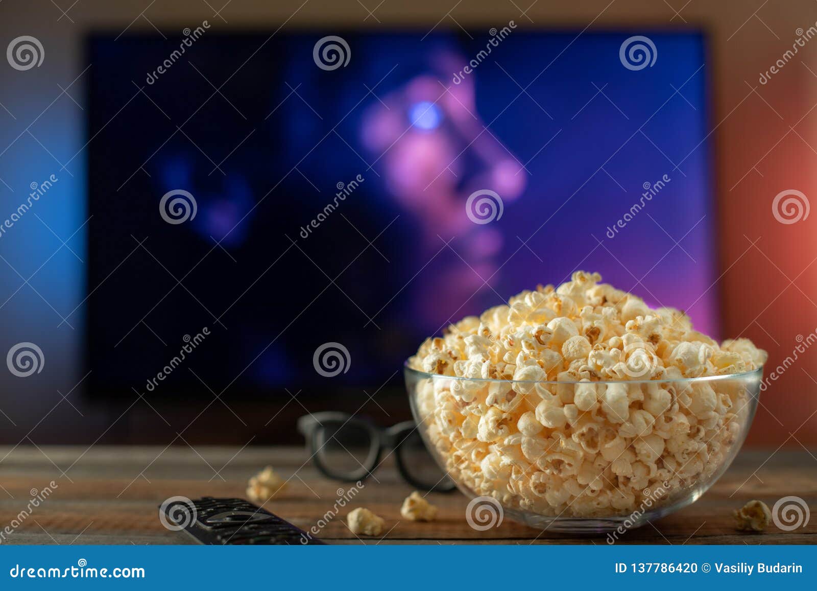 a glass bowl of popcorn, 3d glasses and remote control in the background the tv works. evening cozy watching a movie or tv series